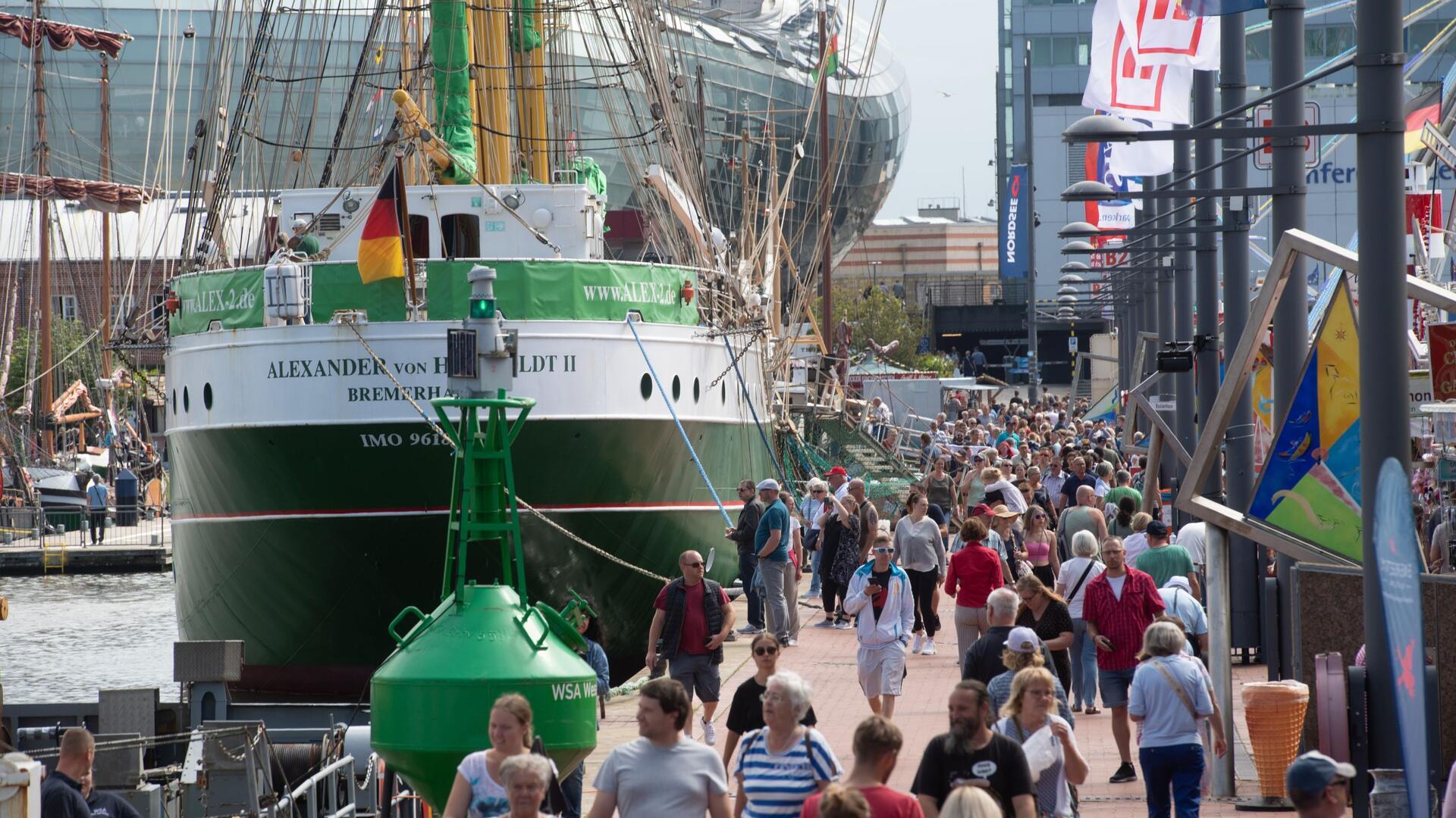 Zahlreiche Menschen laufen auf den Kajen am Neuen Hafen in Bremerhaven an der grün und weiß gestrichenen "Alexander von Humboldt II" vorbei