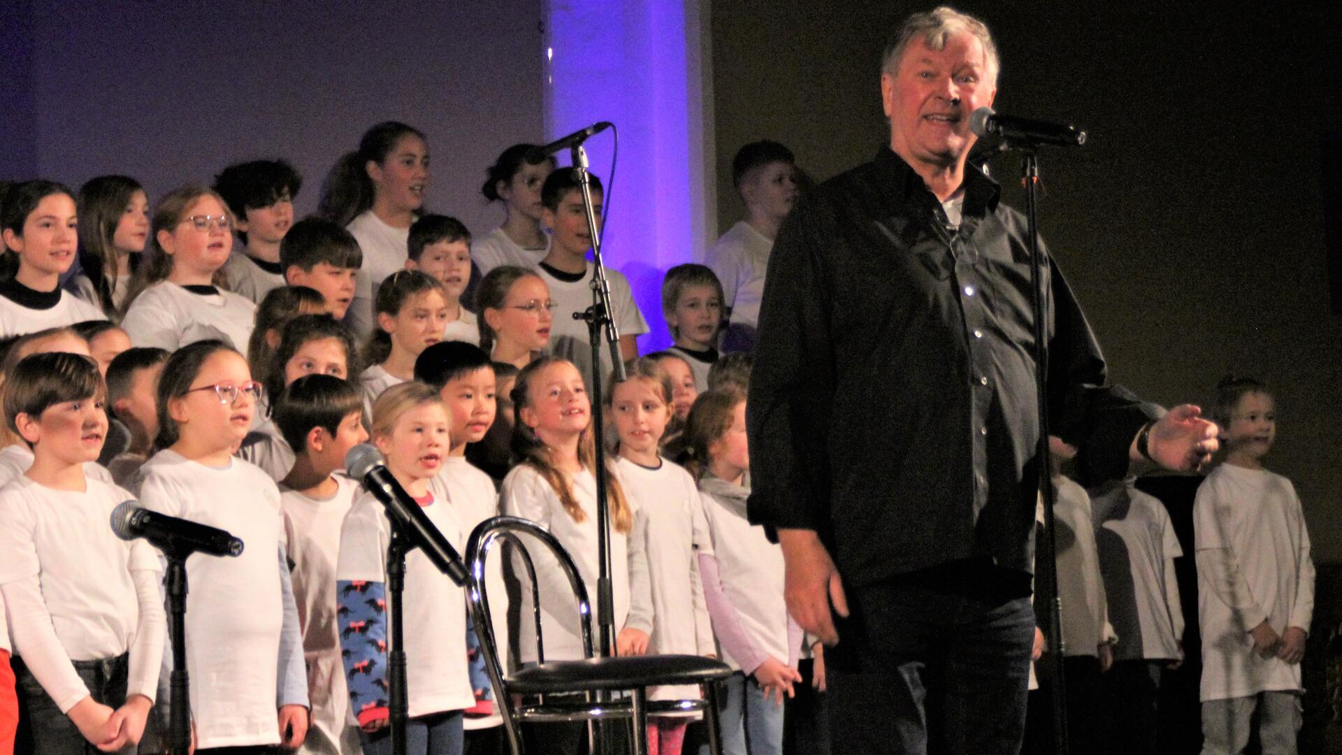 Grundschüler singen in einer Kirche, vorn steht ein Mann, ein Liedermacher