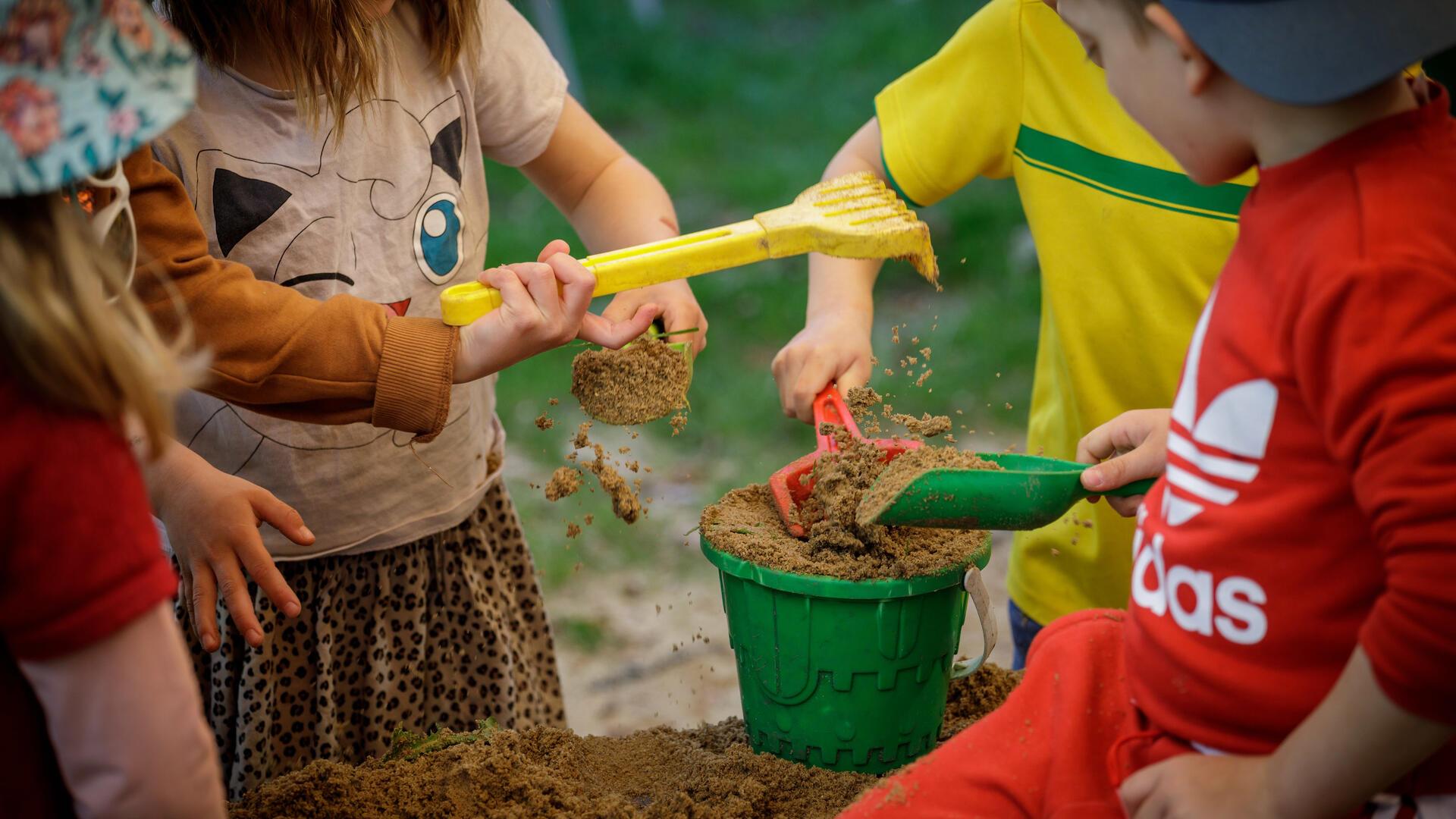 Vier Kinder füllen einen Eimer mit Sand.