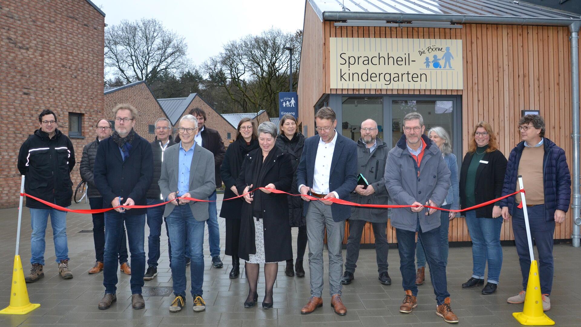 Vertreter der Stadt Zeven, der Börne und der beteiligten Firmen schneiden ein rotes Band vor dem Neubau des Sprachheilkindergartens durch.