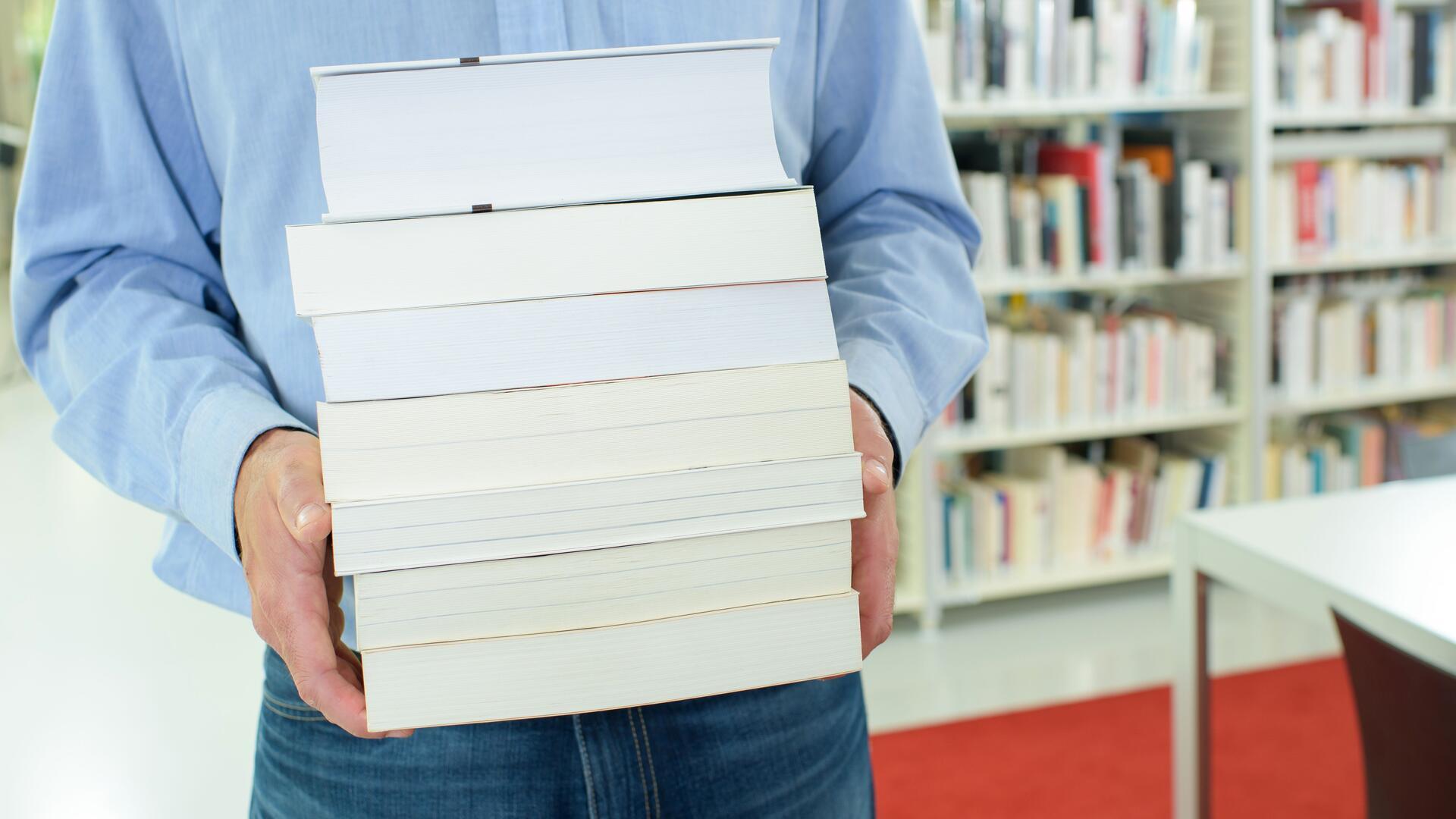 Ein Mann in einem blauen Hemd trägt einen Stapel Bücher.