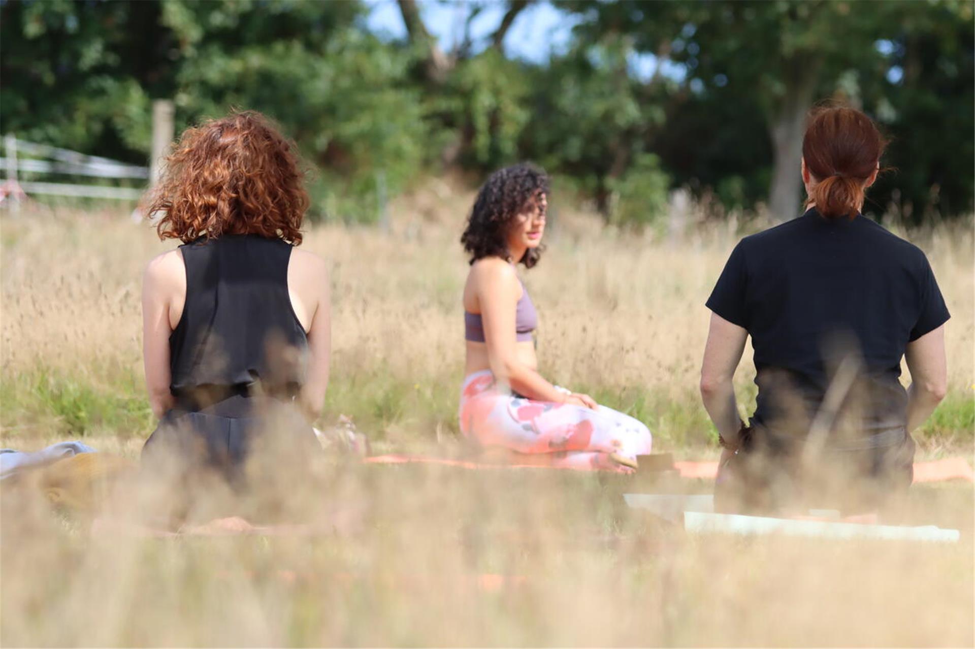 Drei Frauen sitzen auf einer Wiese und praktizieren Yoga.