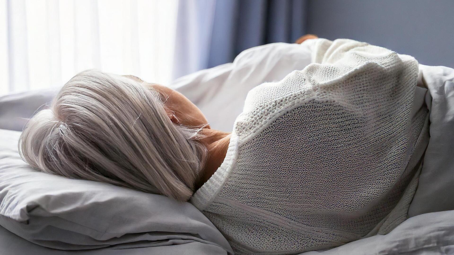 Eine Seniorin mit grauen Haaren liegt auf einem Bett.