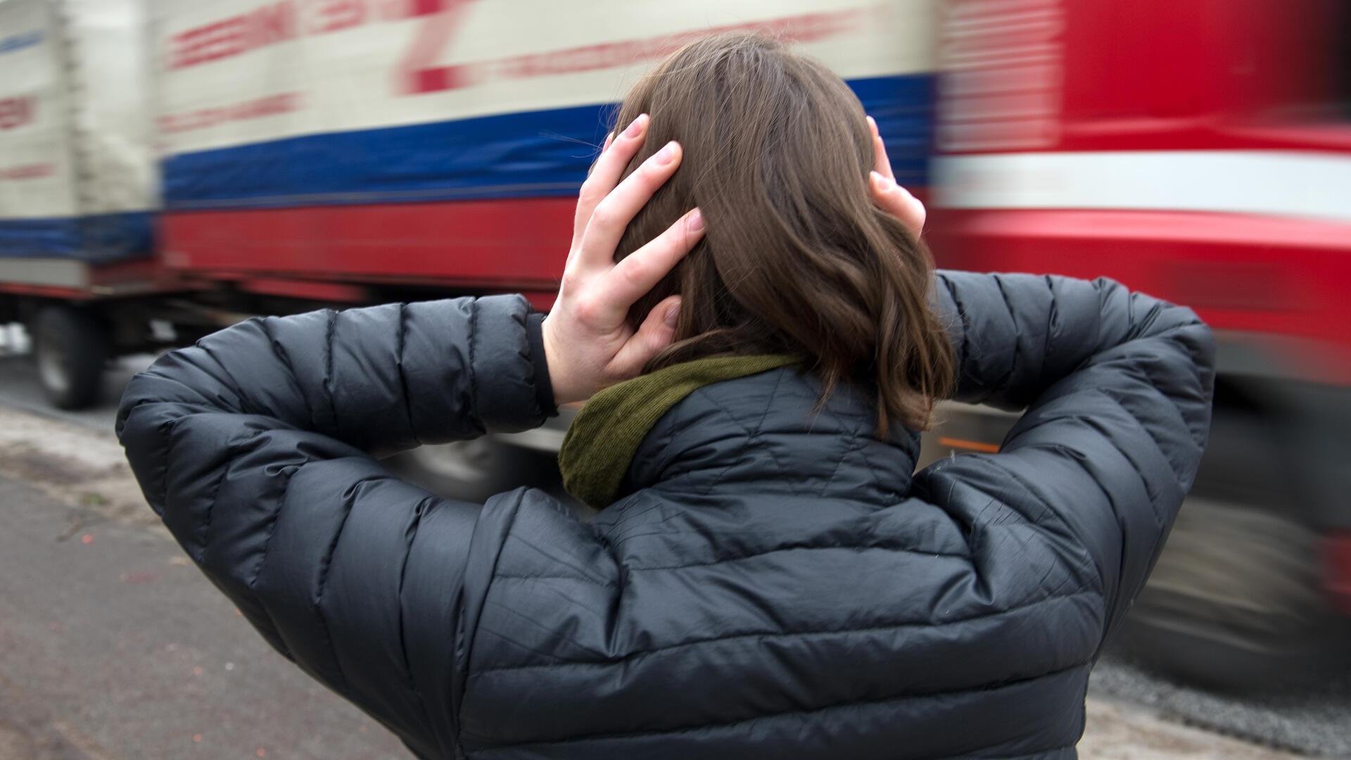  Eine Frau hält sich vor einem nahenden Lastwagen die Ohren zu. 