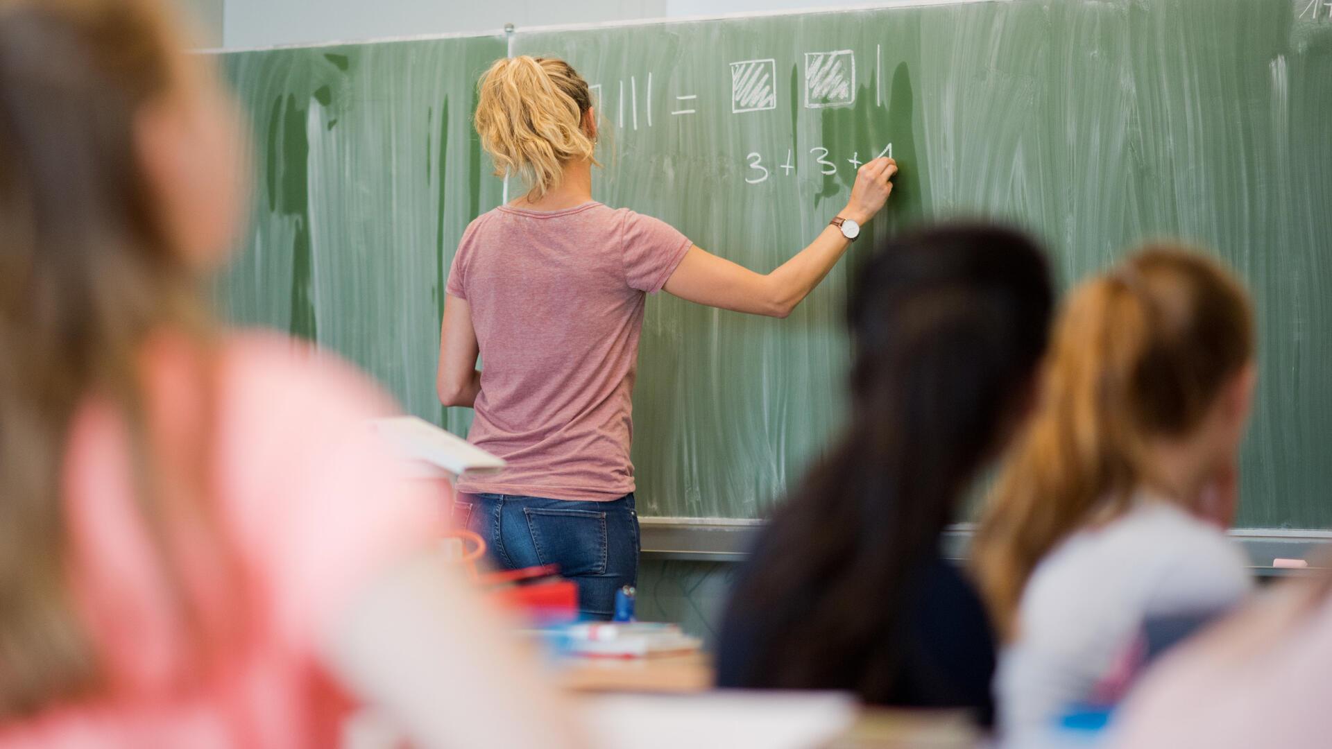 Lehrerin schreibt etwas an die Tafel.