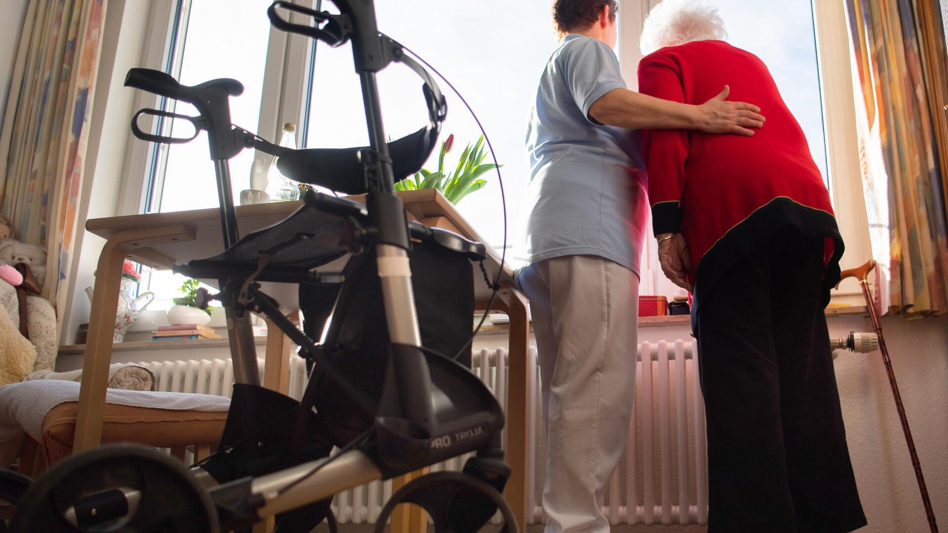 Pflegerin und Seniorin stehen im Pflegeheim am Fenster.