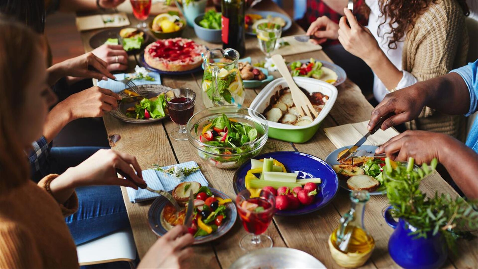 Ein gedeckter Tisch mit vier Paar Händen, die Salat, Gemüse und Brot essen.