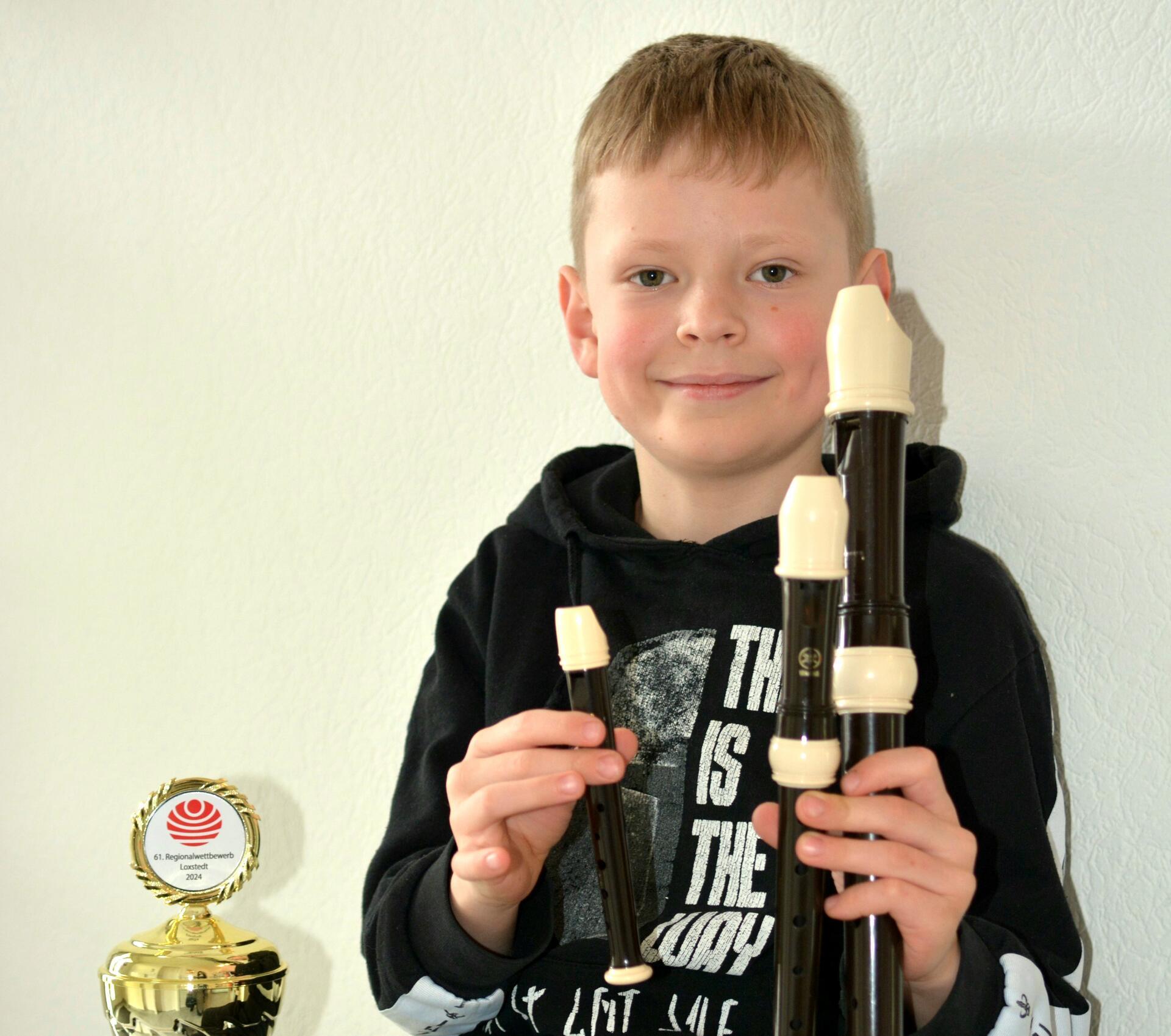 Ein Junge hält drei Blockflöten in der Hand. Neben ihm steht ein Pokal. 