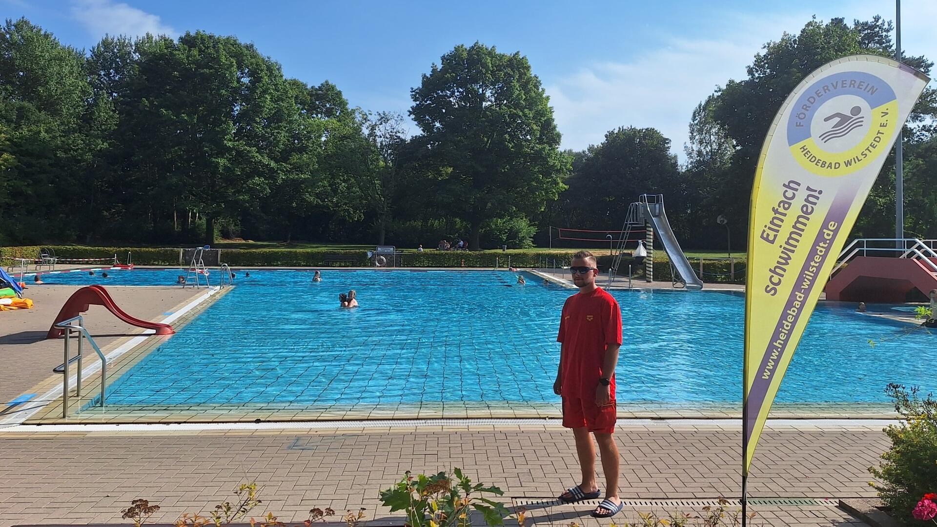 Junger Mann steht vor dem Becken eines Freibades.