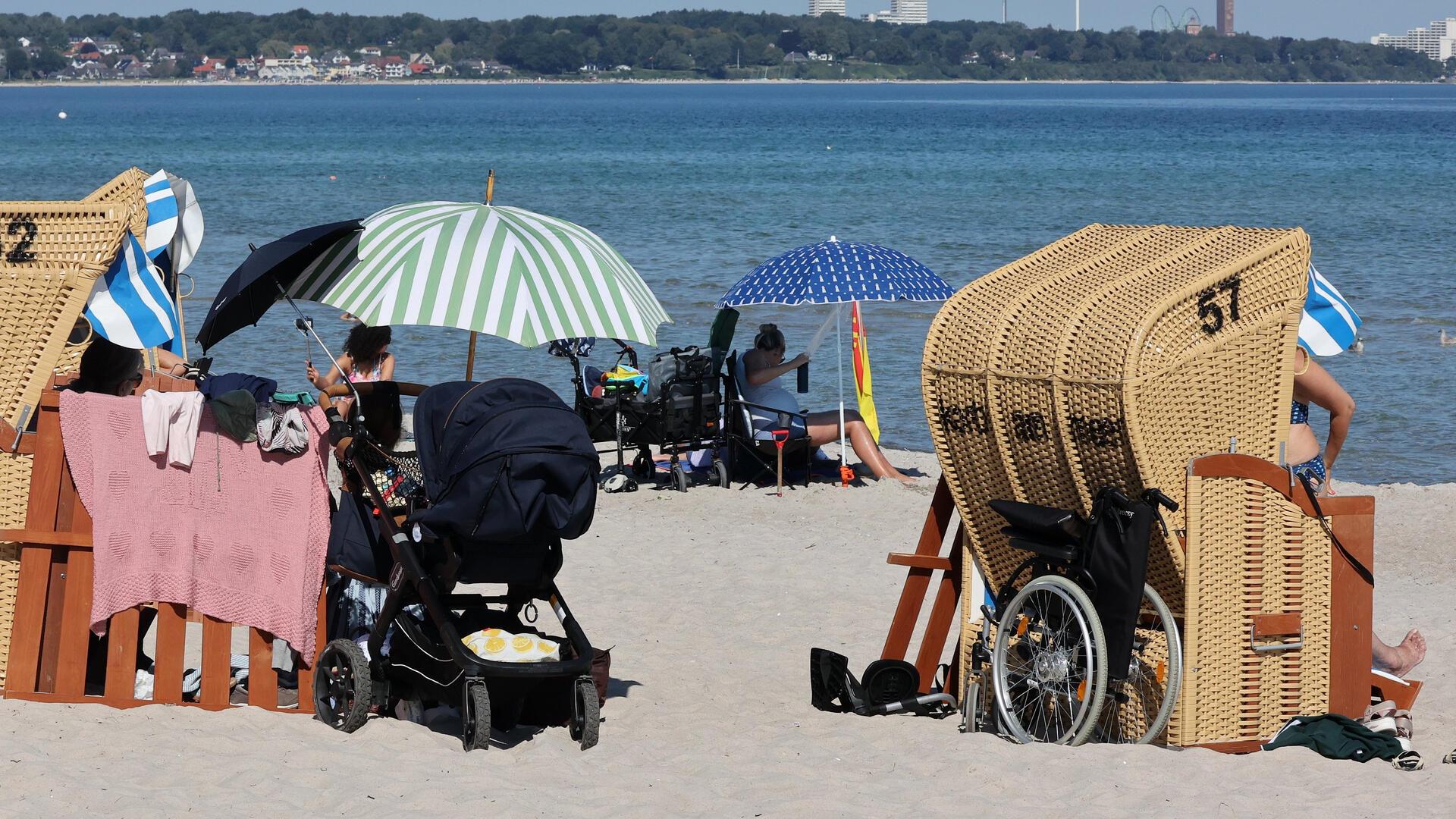 Zwei Strandkörbe am Strand mit einem Rollstuhl und einem Kinderwagen.