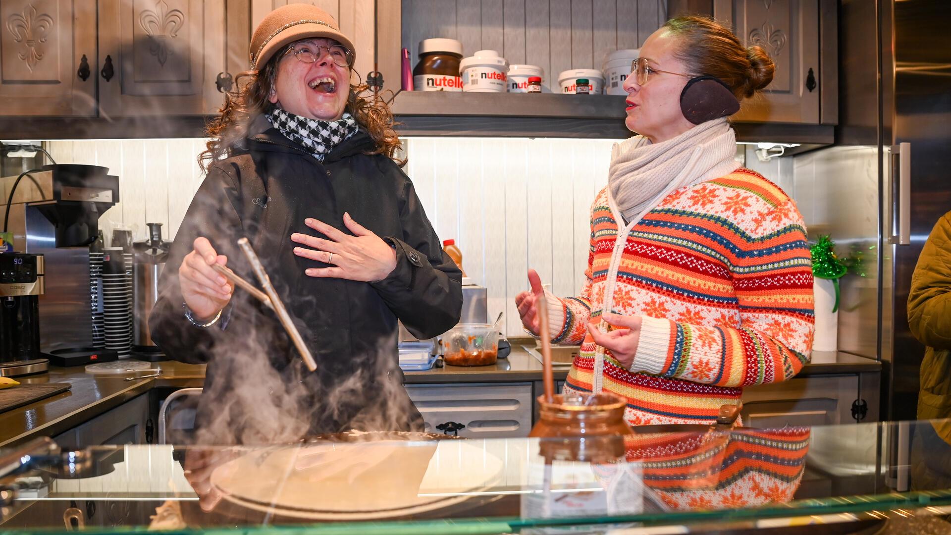 Zwei Frauen in einer Crêpe-Hütte lachen, während sie Crêpes herstellen.