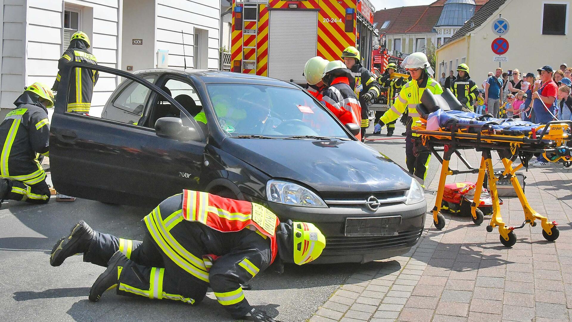 Umringt von Zuschauern arbeiten Rettungskräfte an einem auf der Straße abgestellten Auto. Eine rollende Krankenliege steht bereit. Im Hintergrund stehen mehrere Einsatzfahrzeuge auf der Straße. 