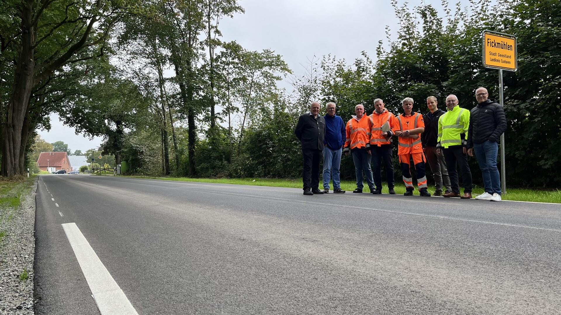 Eine Gruppe von acht Personen steht neben dem Ortsschild von Fickmühlen an einer runderneuerten Straße.