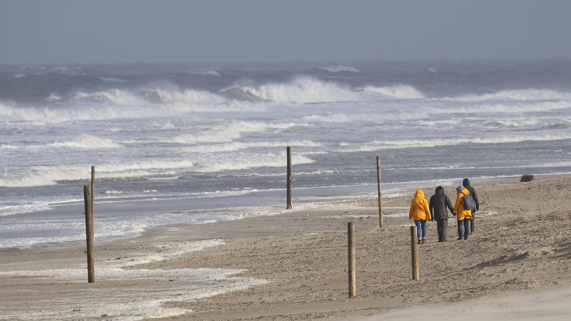 Bei stürmischem Wetter und Wellen gehen Spaziergänger am Strand der Insel Norderney entlang.