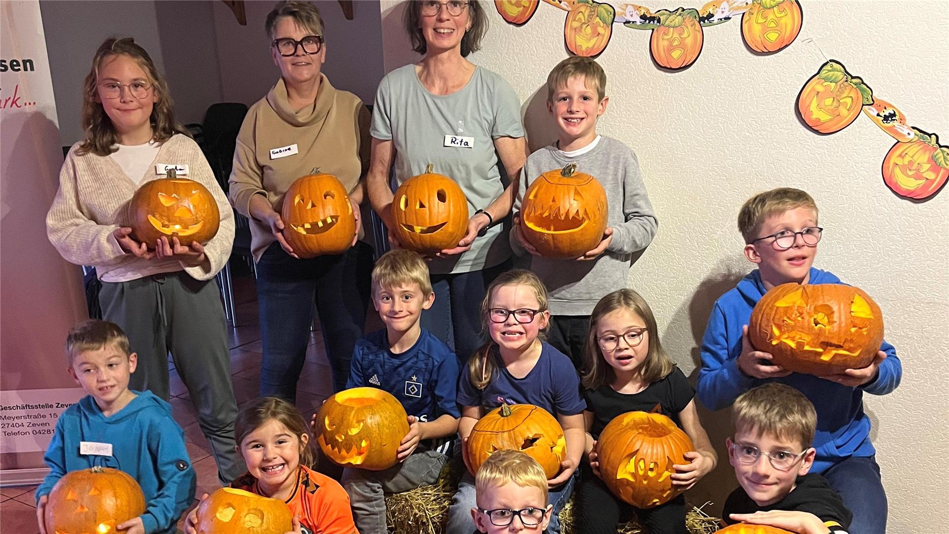 Zwei Frauen und mehrere Kinder halten geschnitzte Kürbisse in die Kamera.