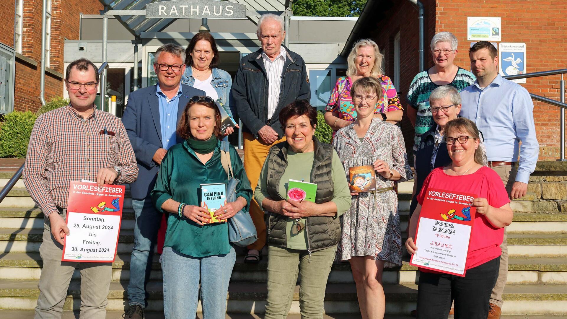 Eine Gruppe von Menschen steht auf den Stufen vor dem Rathaus der Gemeinde Hagen. Manche halten Bücher in Händen, zwei halten Plakate für das Vorlesefieber hoch.