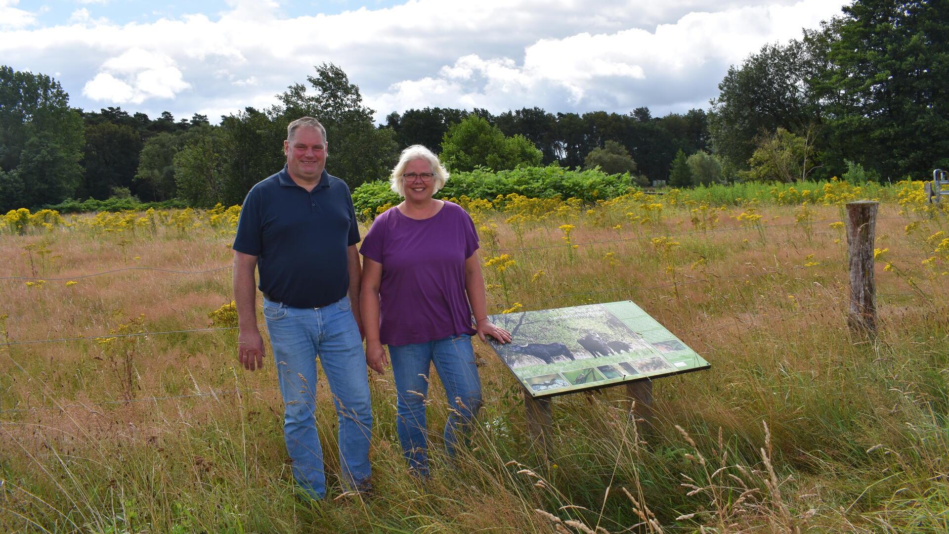 Ein Mann und eine Frau stehen neben einer Hinweistafel vor einer Wiese.