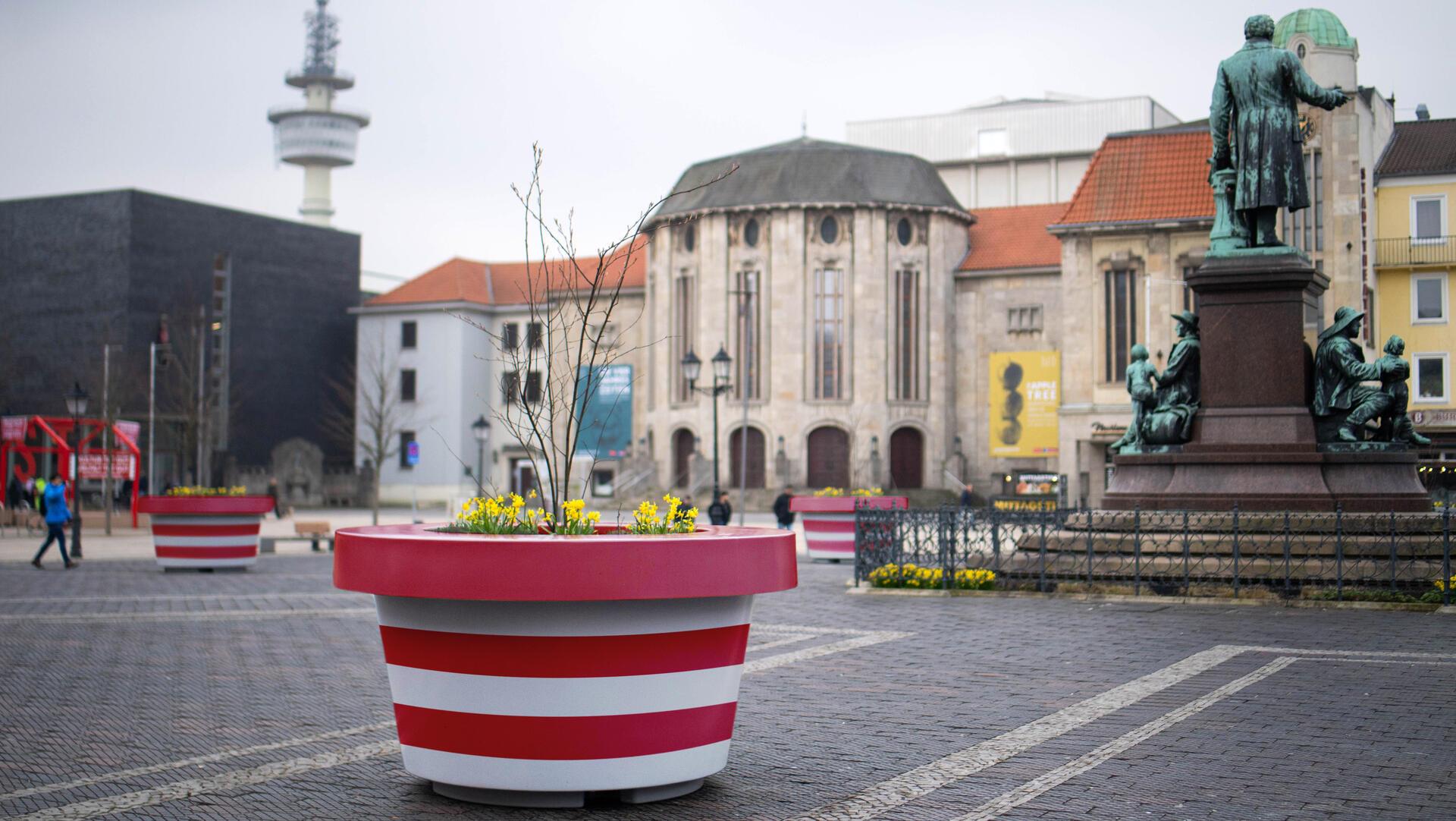 Ein rot-weiß gestreifter Kübel ist auf einem öffentlichen Platz zu sehen. 