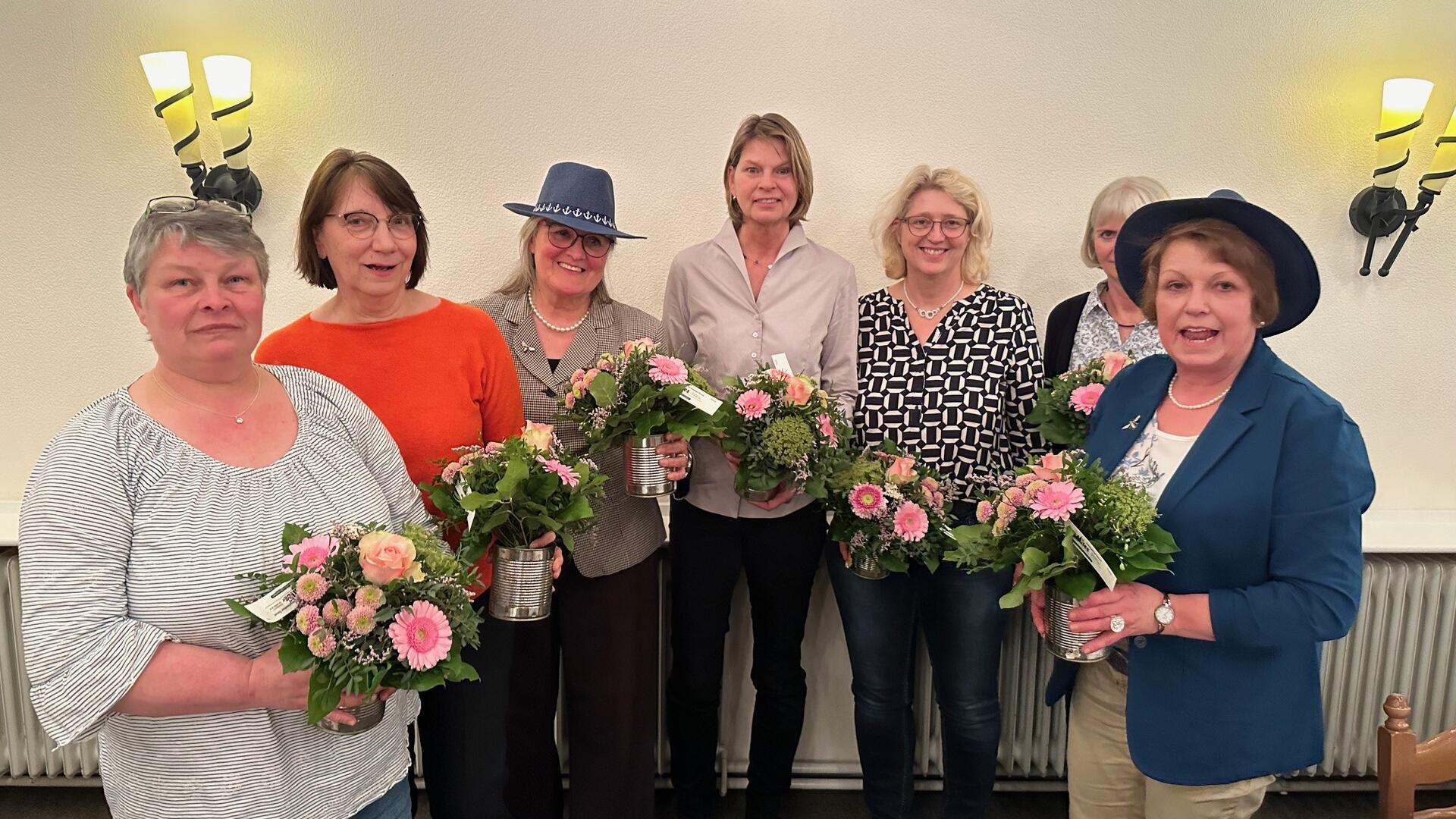 Sieben Frauen stehen im Halbkreis, jede hält einen Blumenstrauß in Händen.