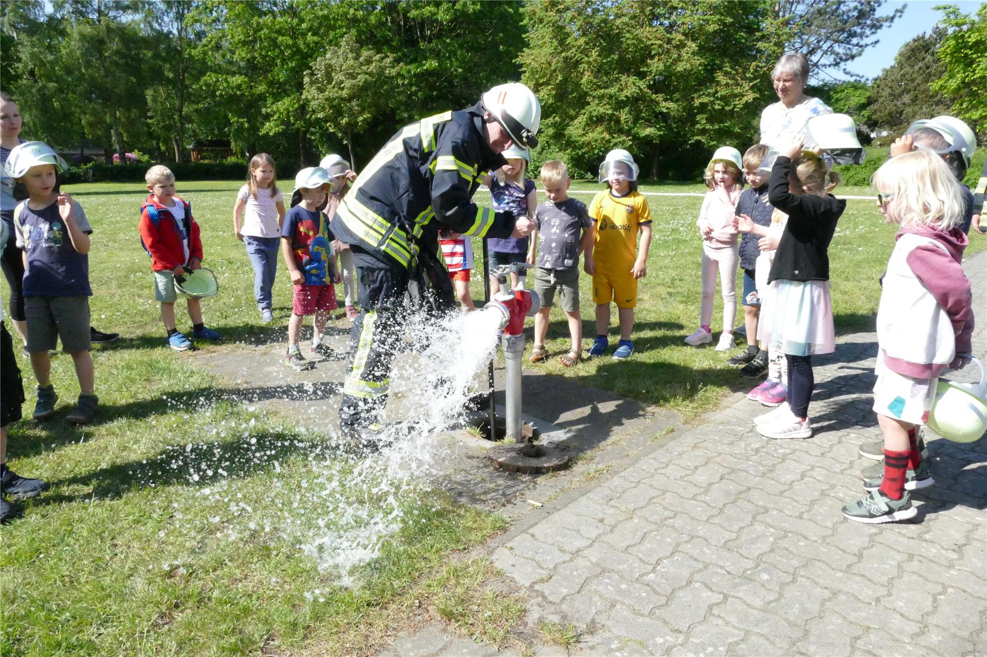 Wasser spritzt aus einem Schlauch. Kinder und Erwachsene schauen zu.