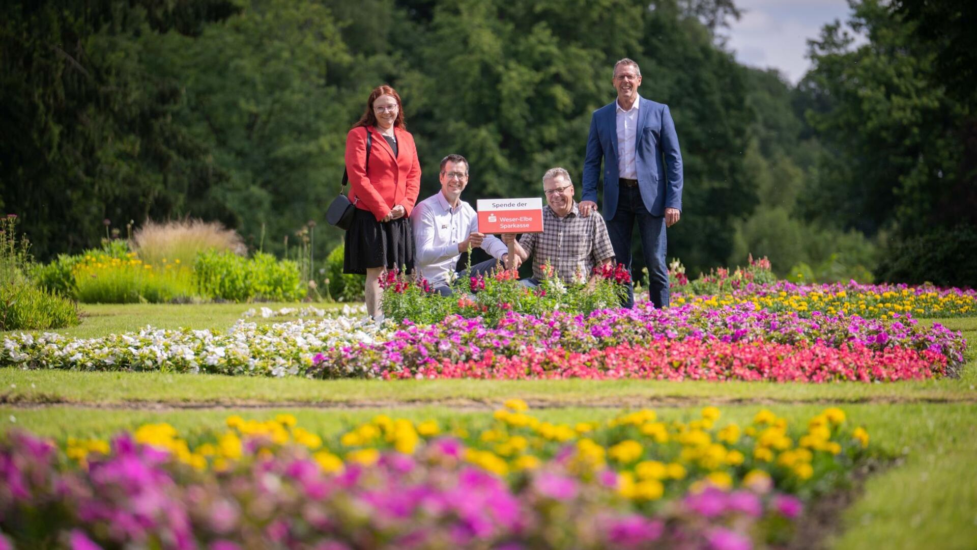 Eine Frau und drei Männer stehen oder knien nebeneinander inmitten bunter Blumenbeete