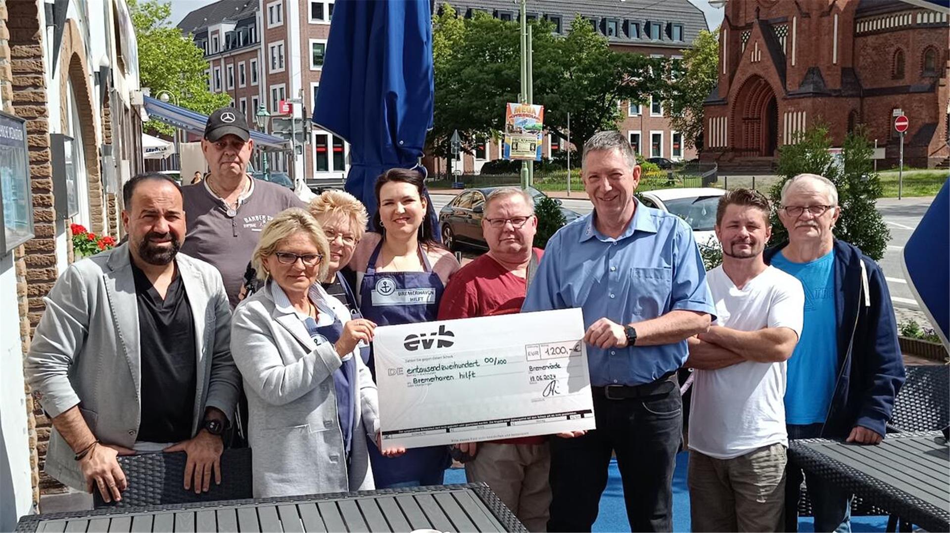 Gruppenfoto von neun Menschen an der Hafenstraße in Lehe. Eine Frau und ein Mann in der Mitte der Gruppe halten gemeinsam einen großen, symbolischen Spendenscheck.