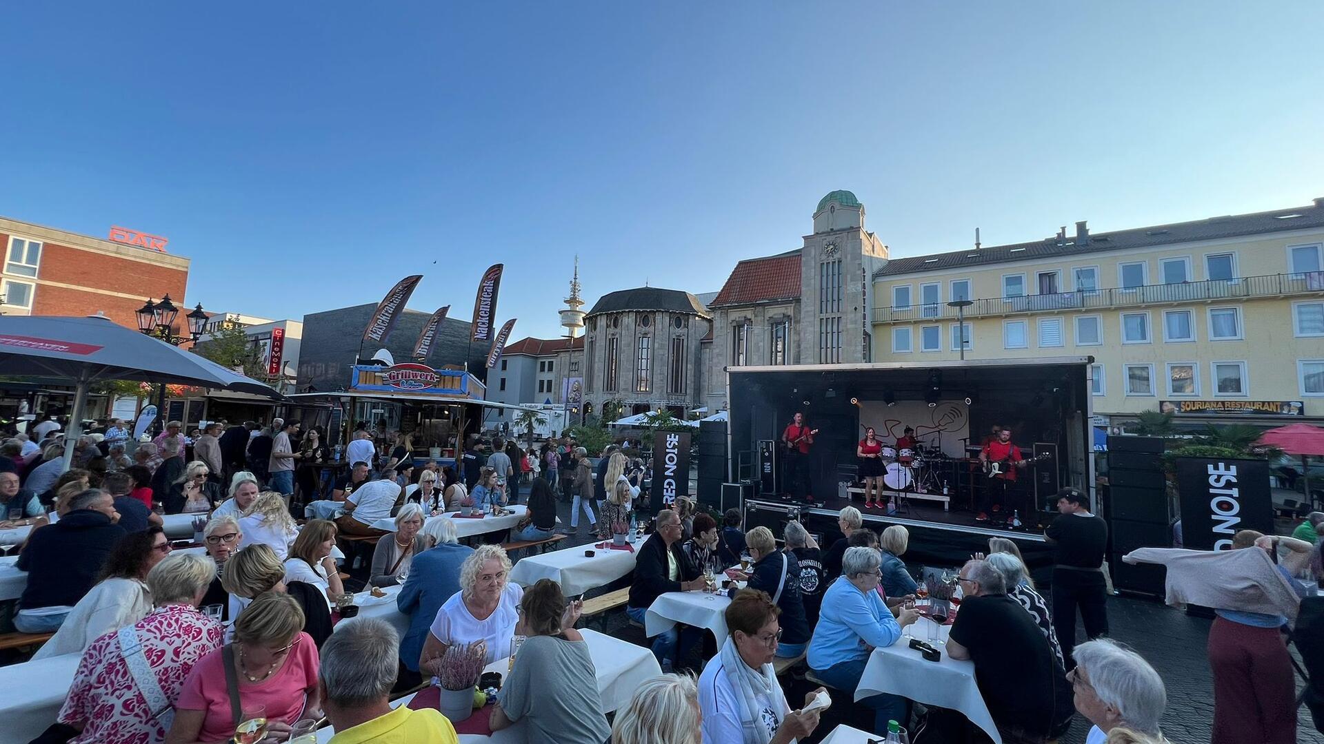 Vielen Menschen sitzen an Tischen vor einer Bühne.