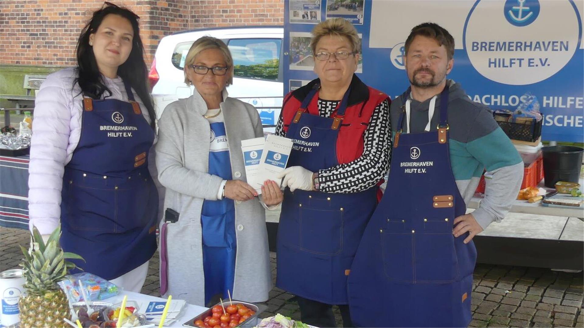 Drei Frauen und ein Mann stehen an einem Stand des Vereins "Bremerhaven hilft".