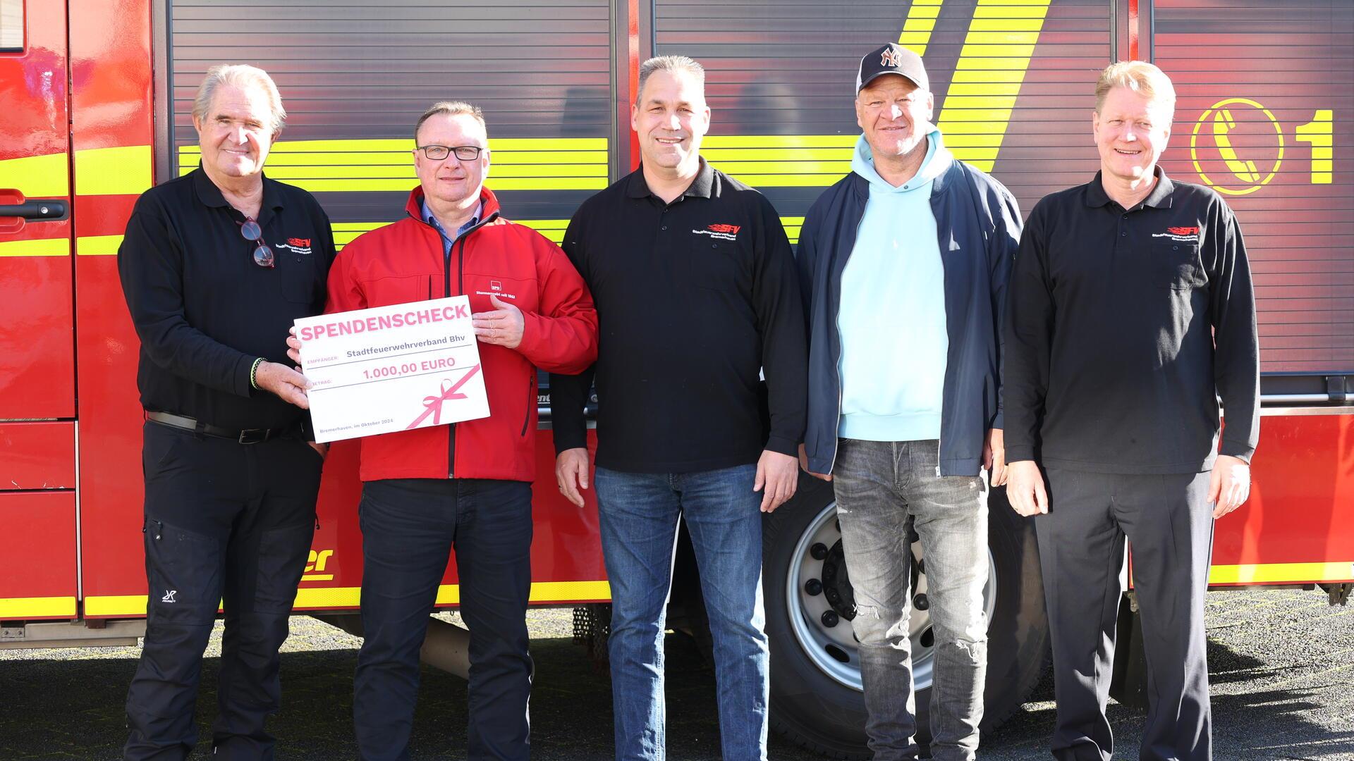 Gruppenfoto mit Spendenscheck Fünf Männer vor einem roten Feuerwehrfahrzeug