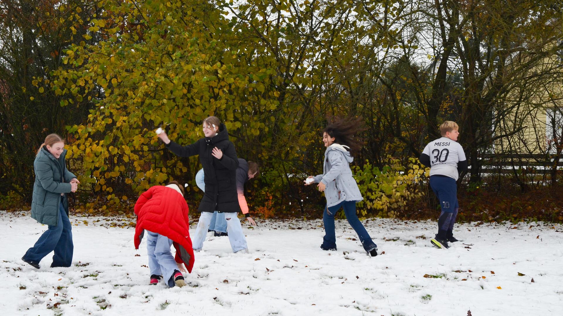 Eine Gruppe von Kindern spielt im Schnee. Sie lachen und bewerfen sich gegenseitig.