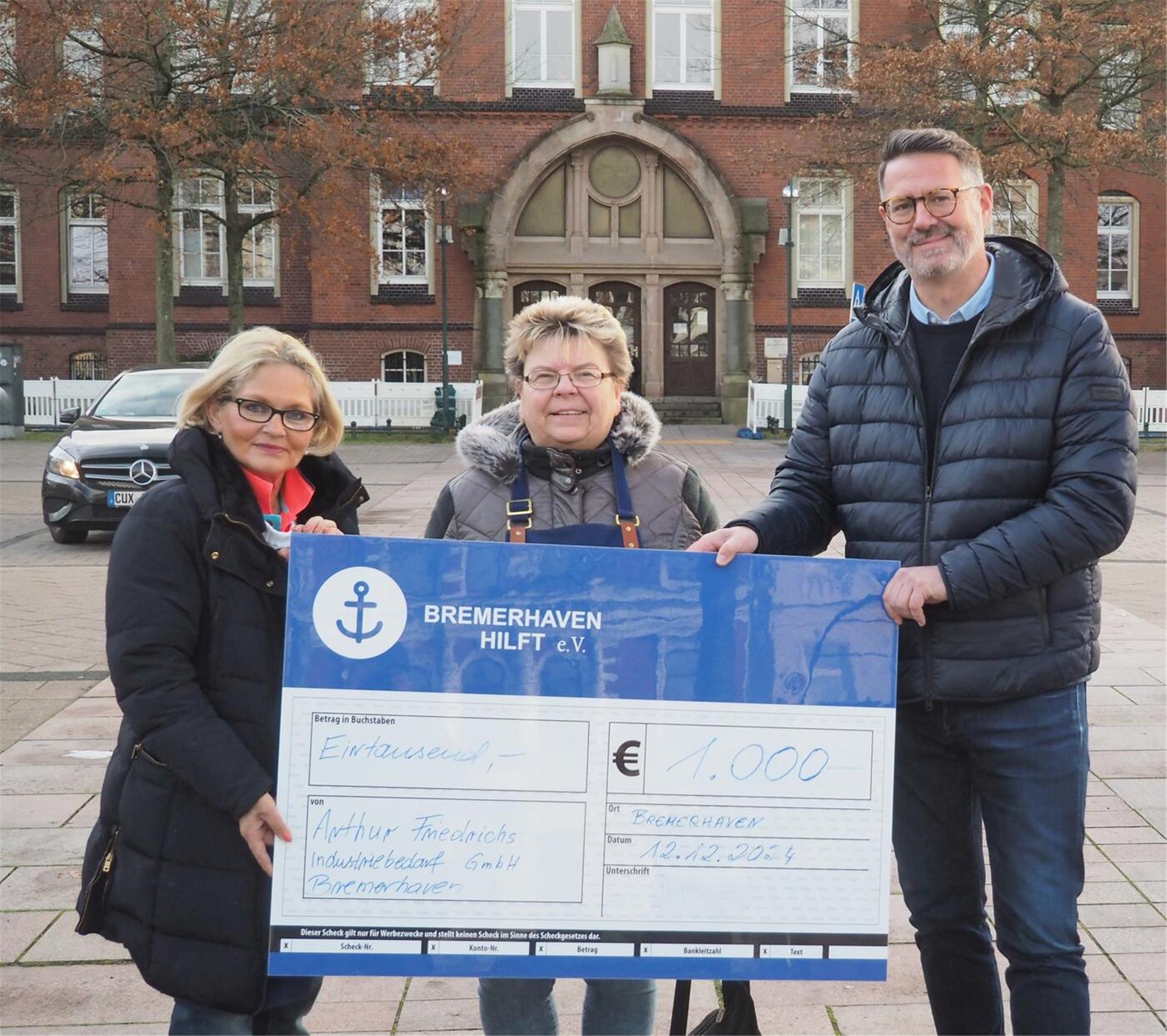 Zwei Frauen und ein Mann halten einen Spendencheck in Händen