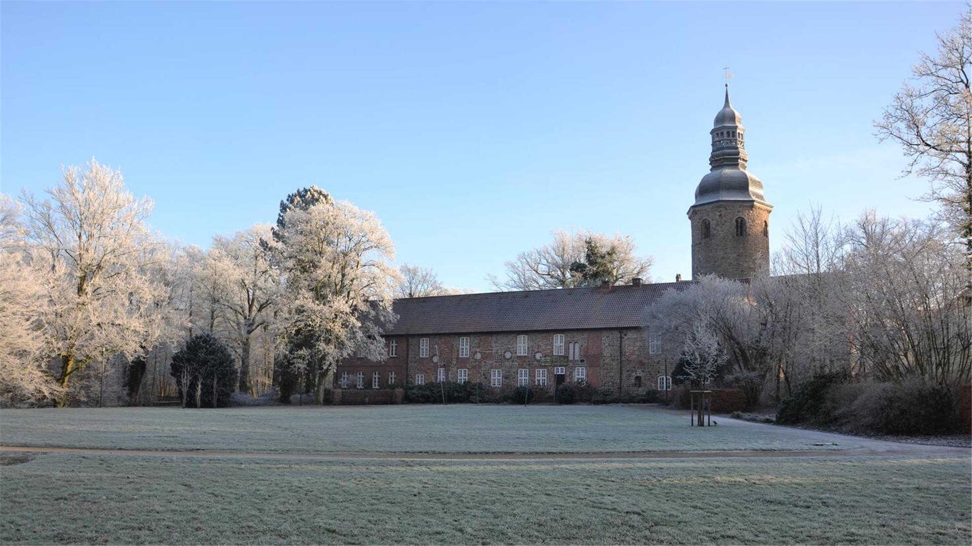 Ein altes Klostergebäude steht in einem Park, dessen Bäume bei Frost weiß in der Sonne strahlen.