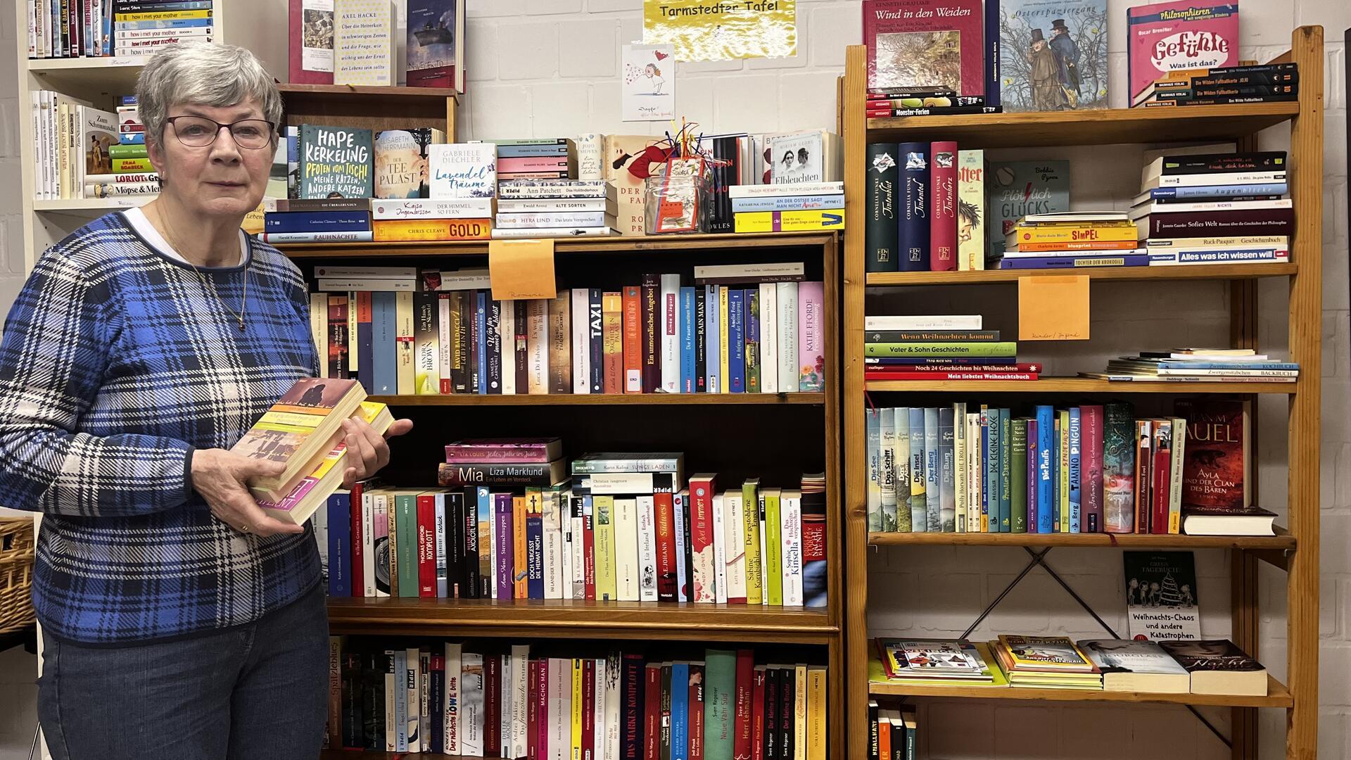 Eine Frau hält Bücher in der Hand und steht vor einem Bücherregal.