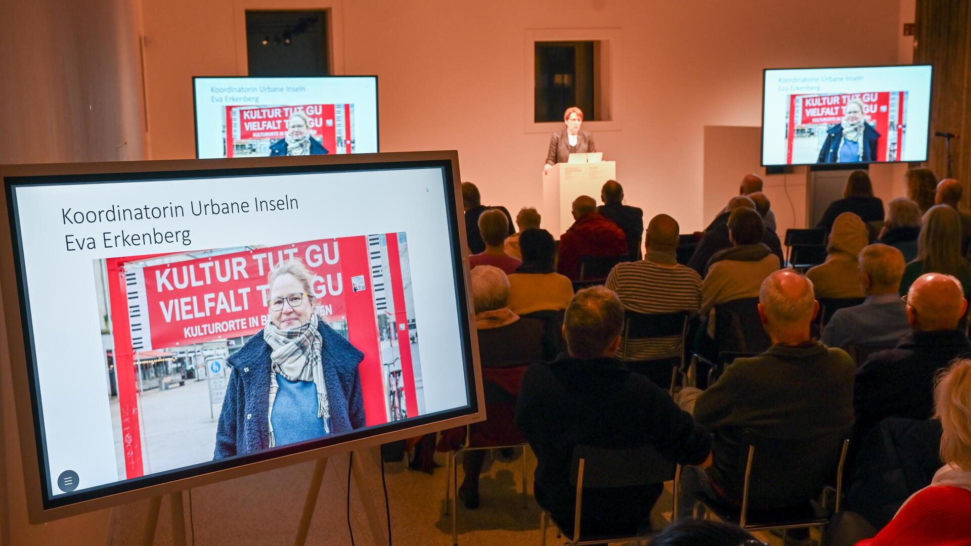 Bürger-Dialog zur Zukunft der Bremerhavener Innenstadt im Auswandererhaus: Dorothee Starke gibt einen Ausblick am Pult, Eva Erkenberg ist auf dem Bildschirm zu sehen.