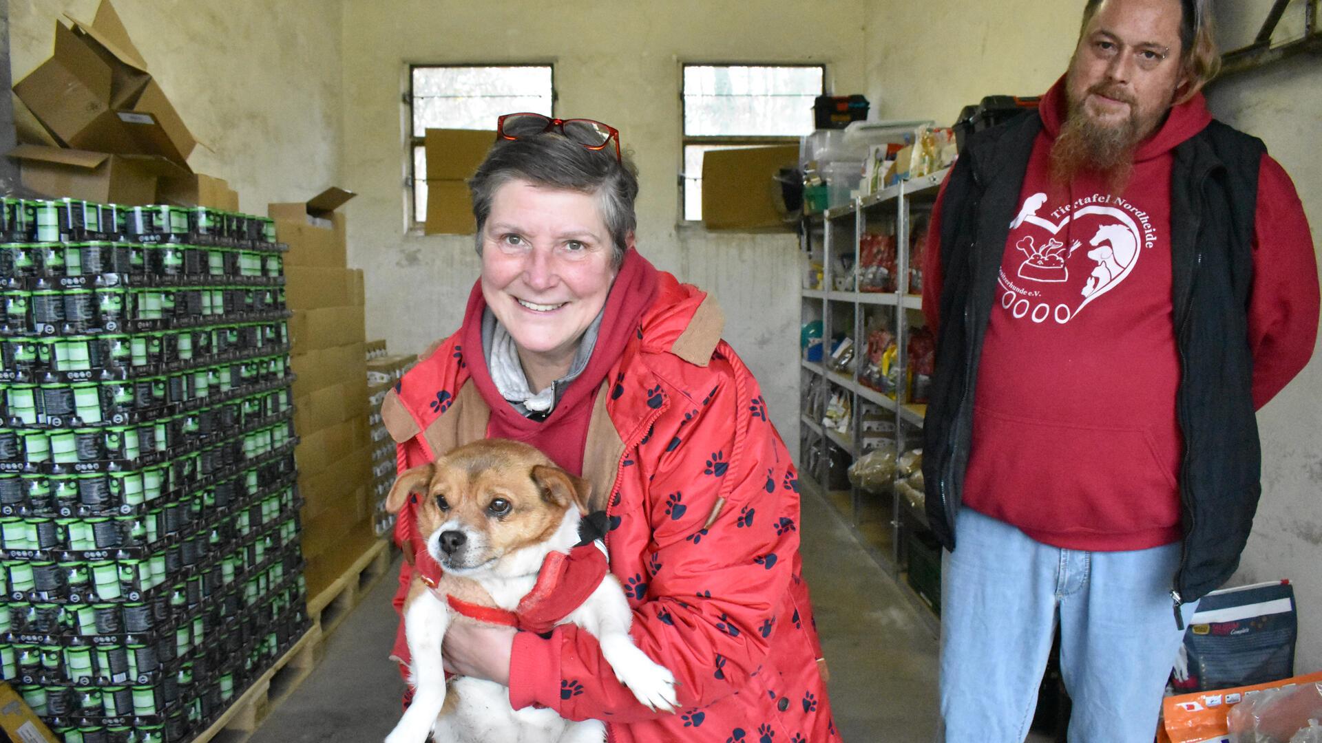 Eine Frau in einer roten Jacke und kurzen Haaren hält einen kleinen Hund im Arm.