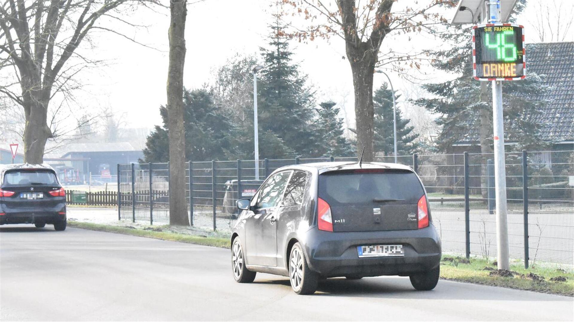 Zwei Autos auf einer Straße vor einem Geschwindigkeitsmessgerät.