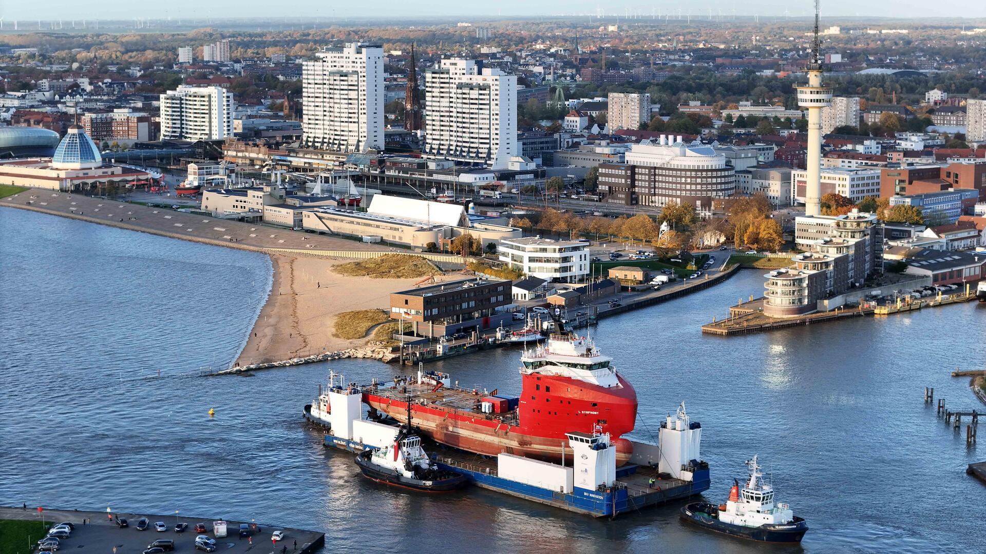 Ein Ponton, beladen mit einem Schiff, vor der Skyline Bremerhavens.