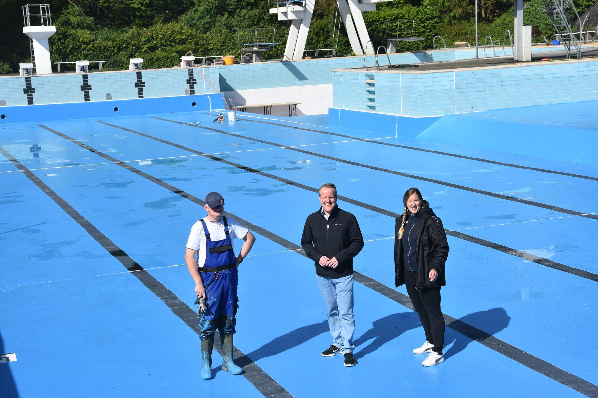 Das Foto zeigt drei Personen in einem leeren Schwimmbbecken. 