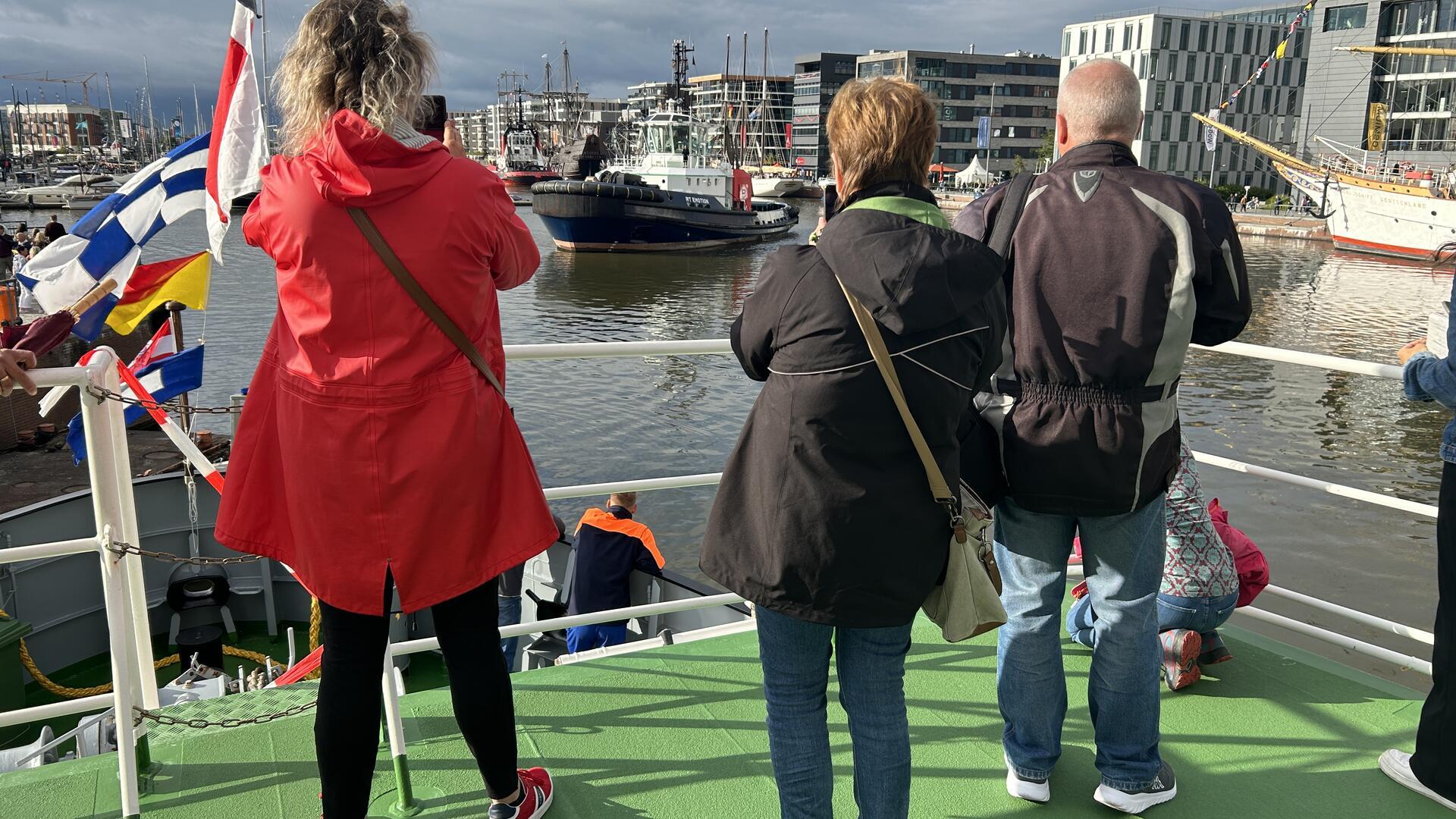 Drei Personen stehen an Bord eines Schiffes und fotografieren das Wendemanöver eines weiteren Schiffes im Neuen Hafen Bremerhaven.