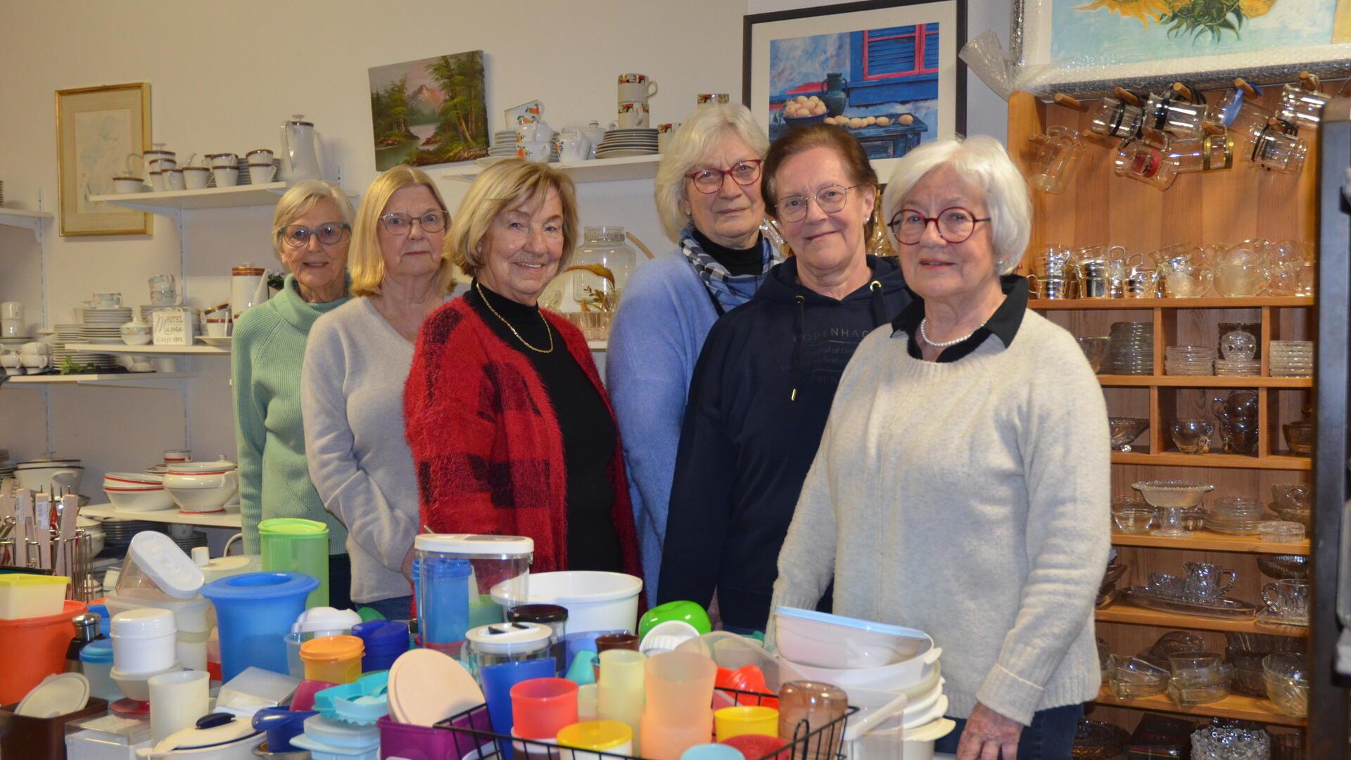 Fünf Frauen stehen zwischen Plastiktöpfen, Geschirr und Gläsern und lächeln in die Kamera.