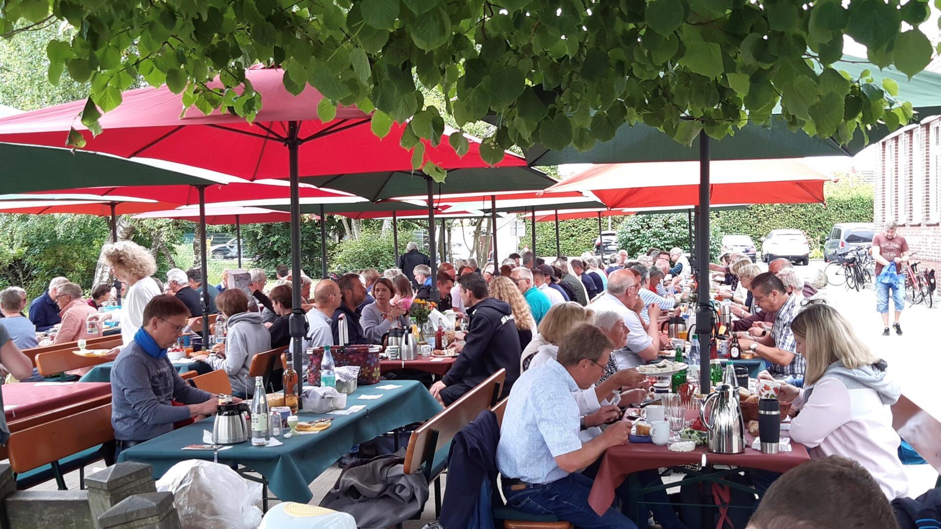 Frauen und Männer sitzen an Biertischgarnituren.