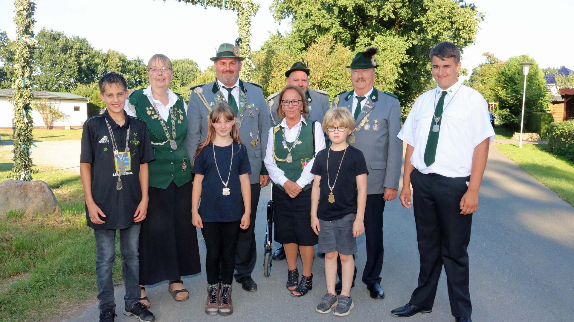 Mehrere Erwachsene in Tracht und Uniform sowie drei Kinder stehen im Freien vor einem Baum.