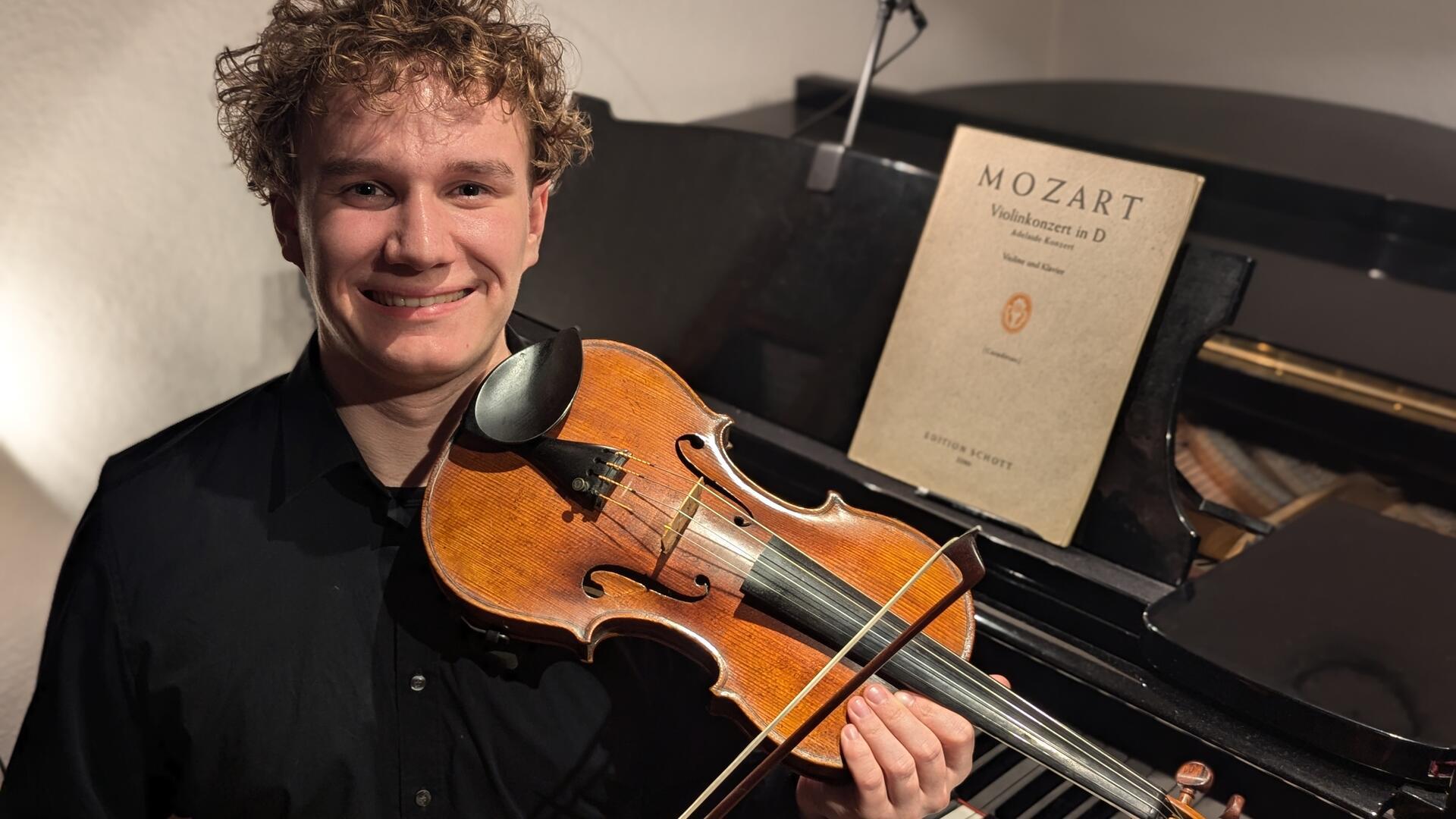 Ein junger Mann mit einer Violine, vor einem Flügel sitzend