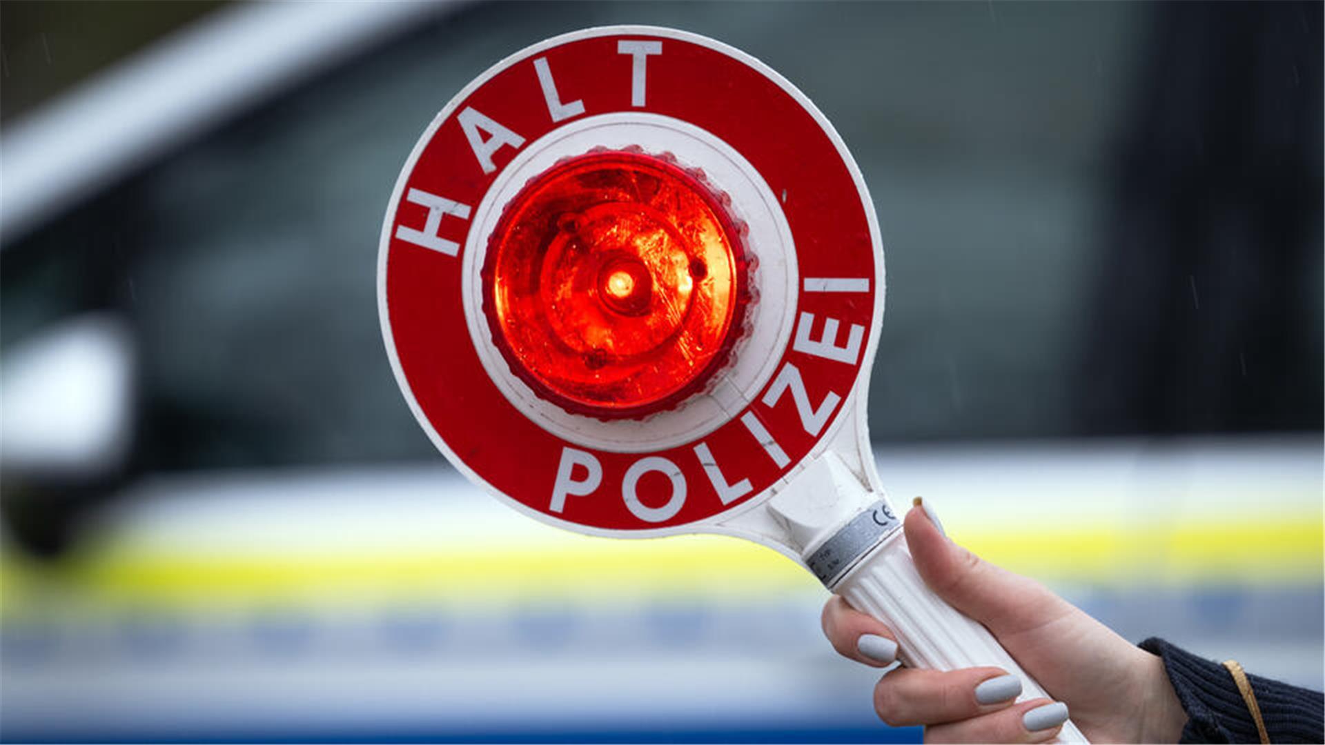 Eine Polizistin hält während einer Verkehrskontrolle eine Polizeikelle mit der Aufschrift "Halt Polizei"