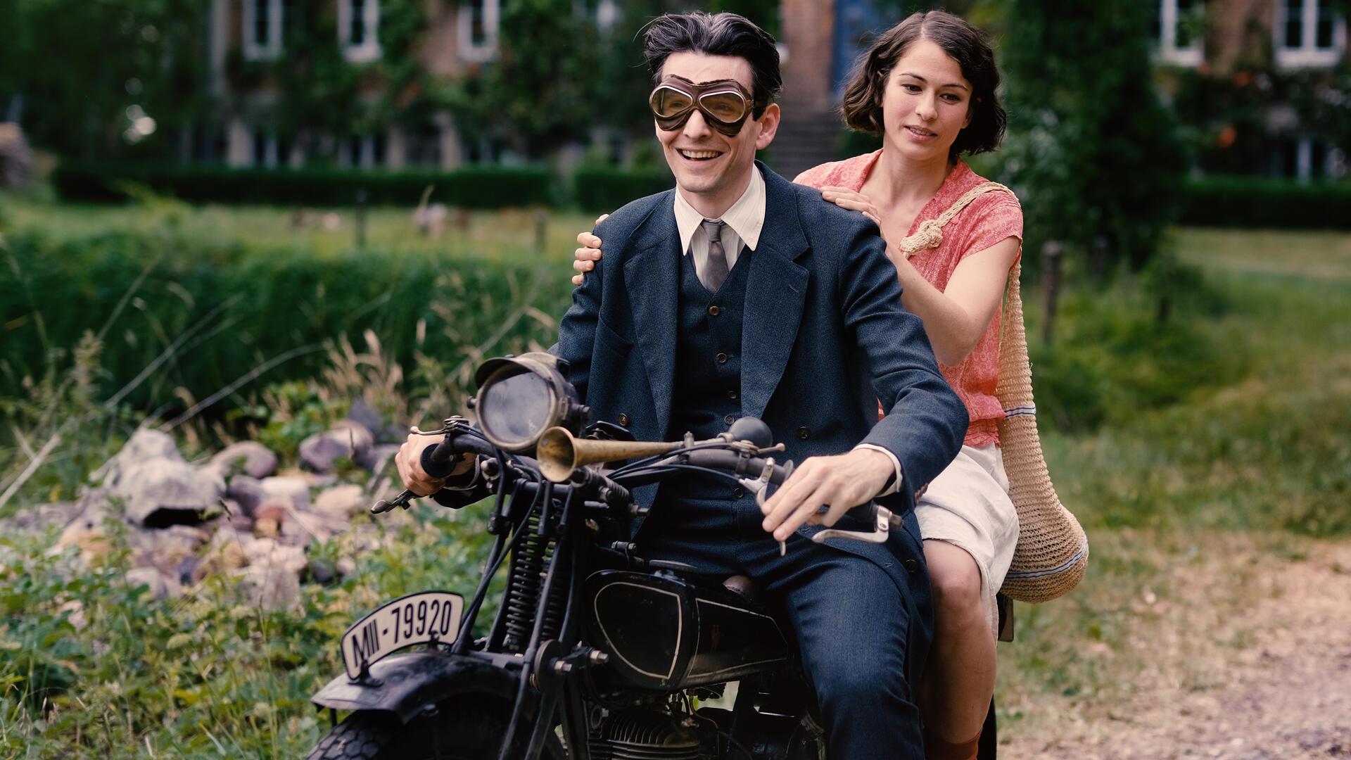 Ein Mann und eine Frau auf einem historischen moped:  Sabin Tambrea als Franz Kafka und Henriette Confurius als Dora Diamant in einer Szene des Films "Die Herrlichkeit des Lebens" 