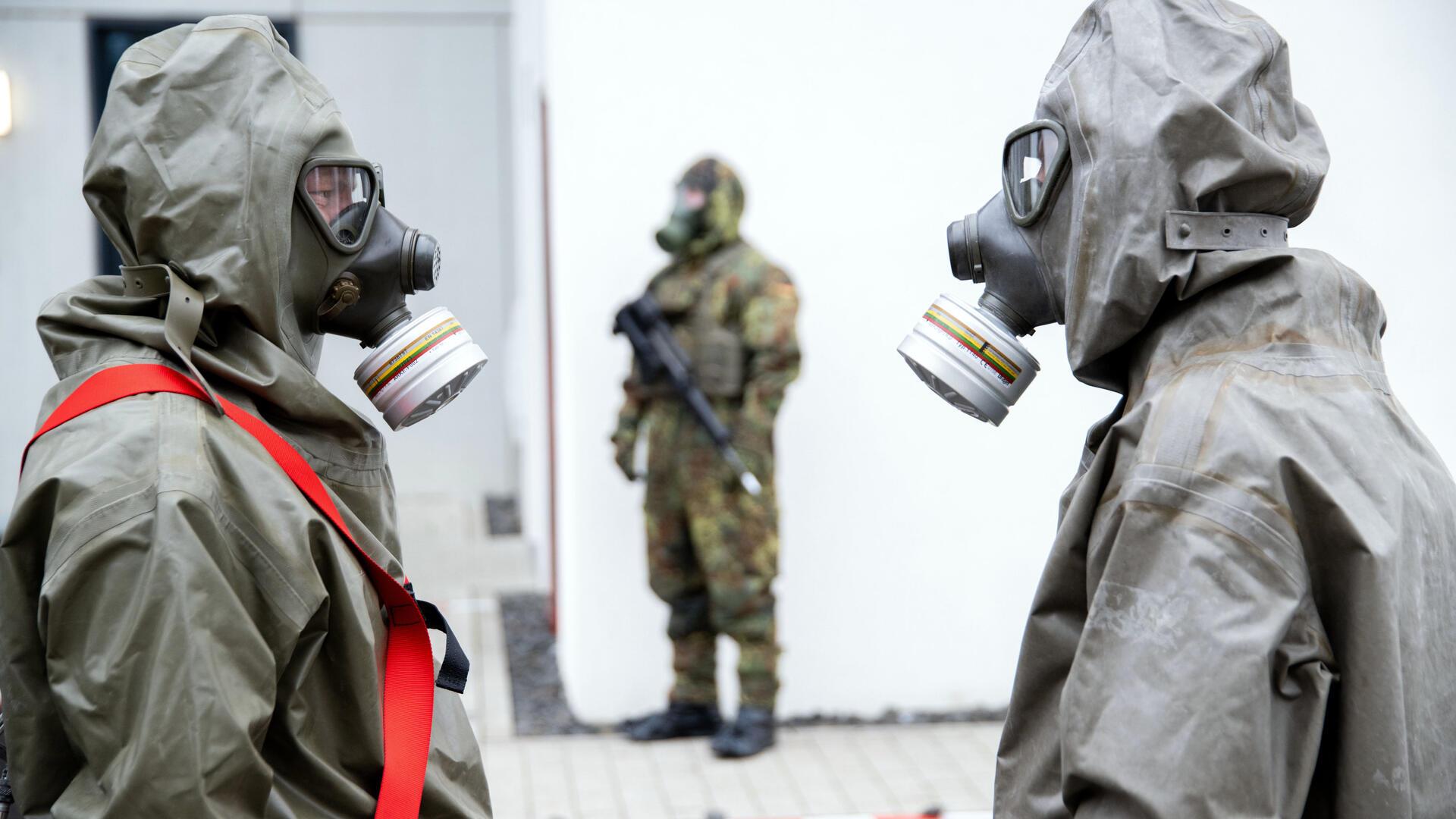  Zwei Soldaten in Schutzanzügen mit Atemmasken stehen sich gegenüber. 