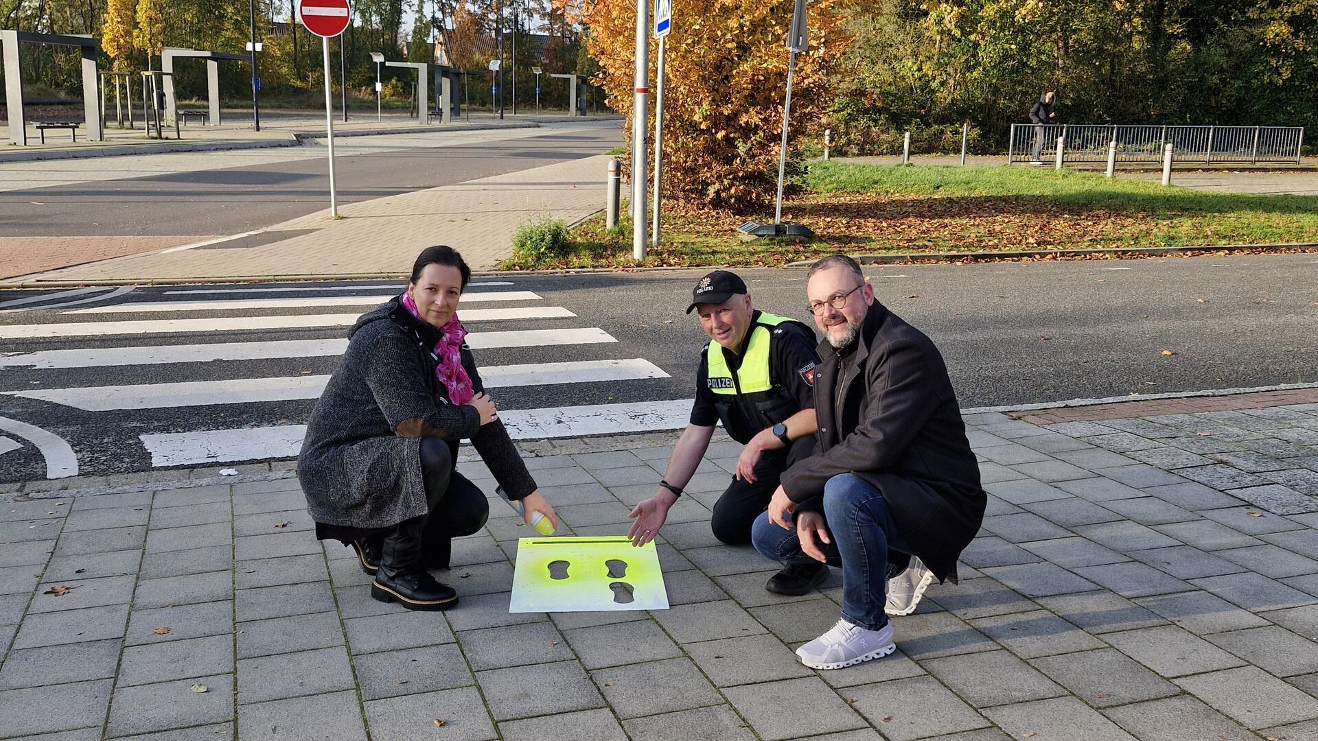 Eine Frau und zwei Männer halten ein Plakat mit schwarzen Fußabdrücken auf gelbem Grund in die Kamera.