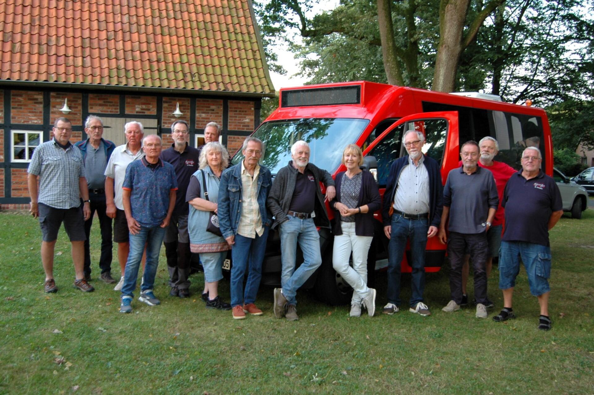 Eine Gruppe Frauen und Männer steht vor einem roten Kleinbus.