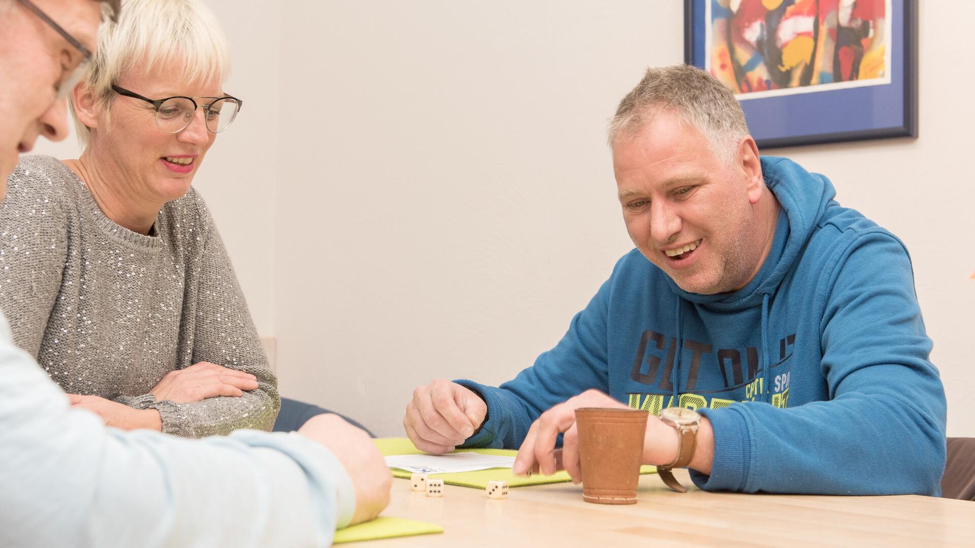 Rechts ein Mann mit einem blauen Pullover, links eine Frau mit einer Brille und ein Mann mit einer Brille 