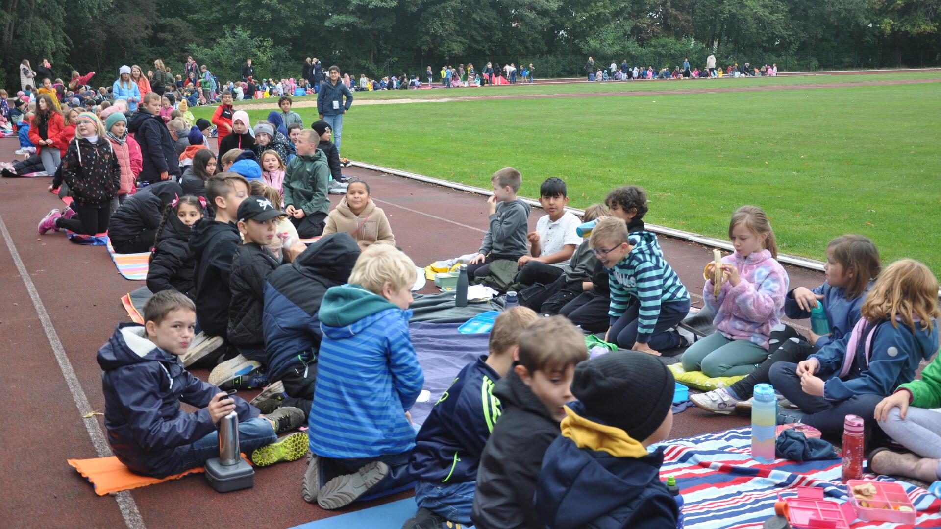 Die Grundschulen picknicken gemeinsam auf dem Sportplatz.